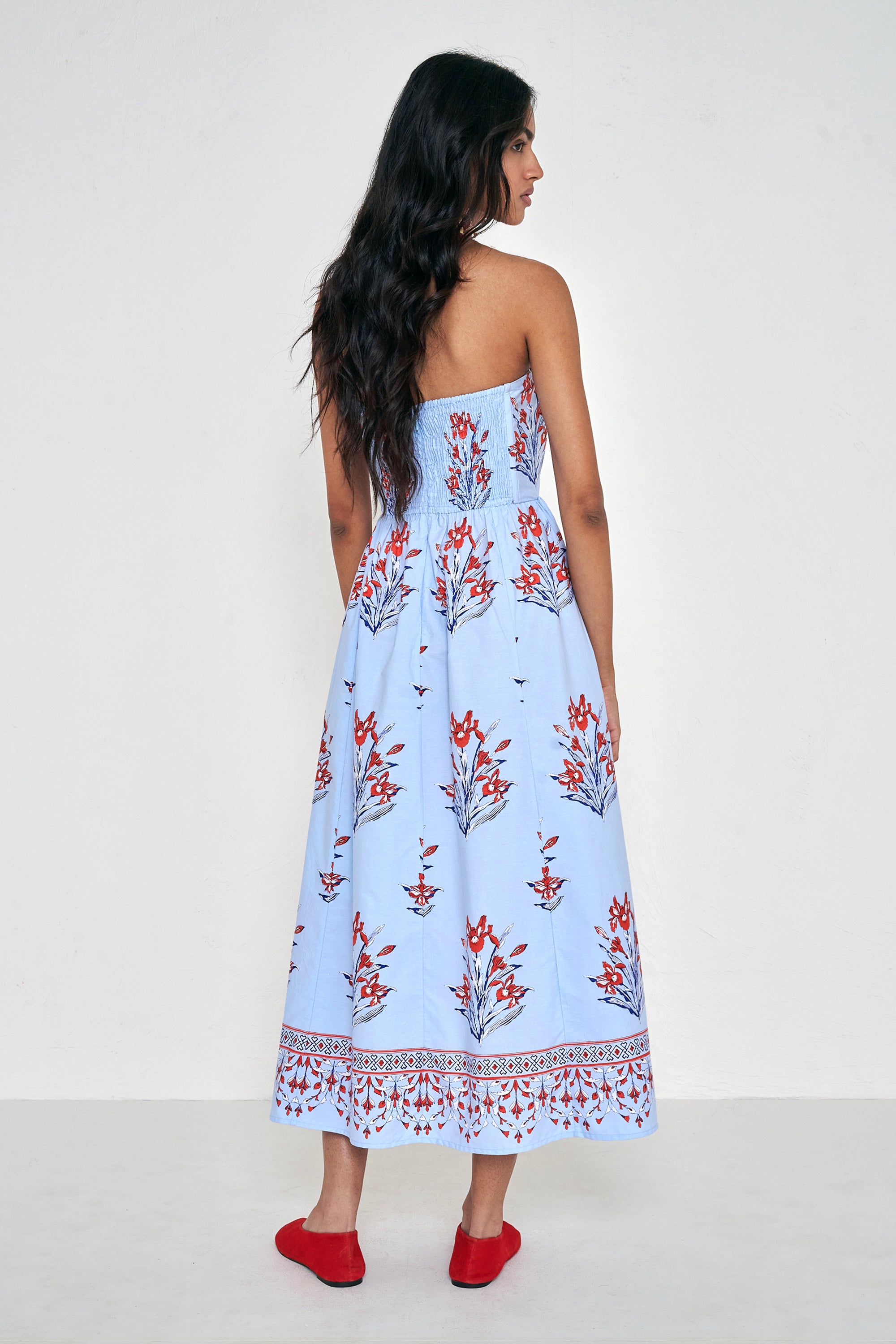 Back view of woman standing. She is wearing the Simona dress in the Brigitte floral print, featuring a strapless bodice, full gathered skirt, and red, white, and blue iris motifs.