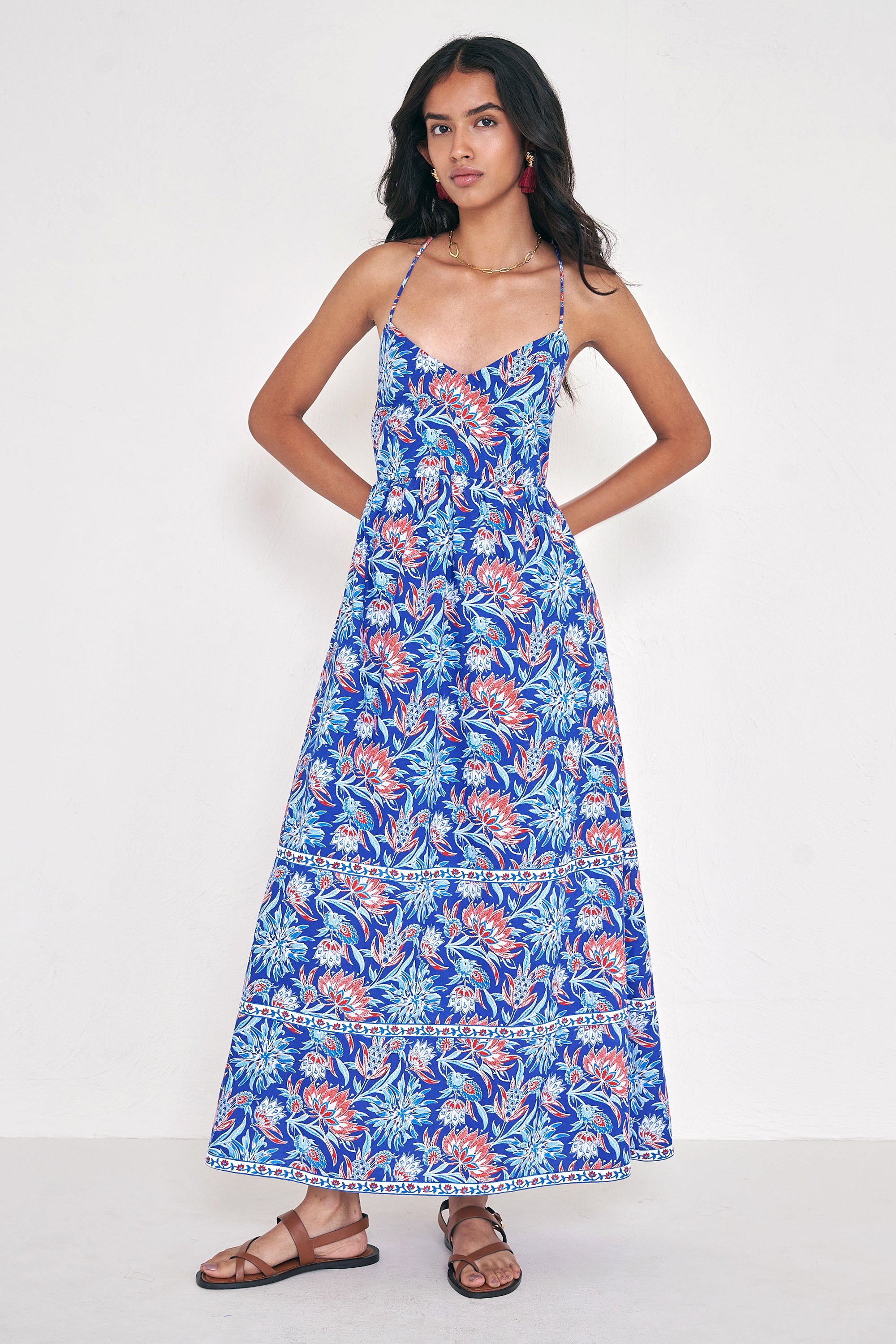 Front view of woman standing. She is wearing the Sofia dress in the Philippa print, featuring a strappy sundress silhouette, gathered ankle-length skirt, and red, white, and blue wildflower motifs inspired by Provence.