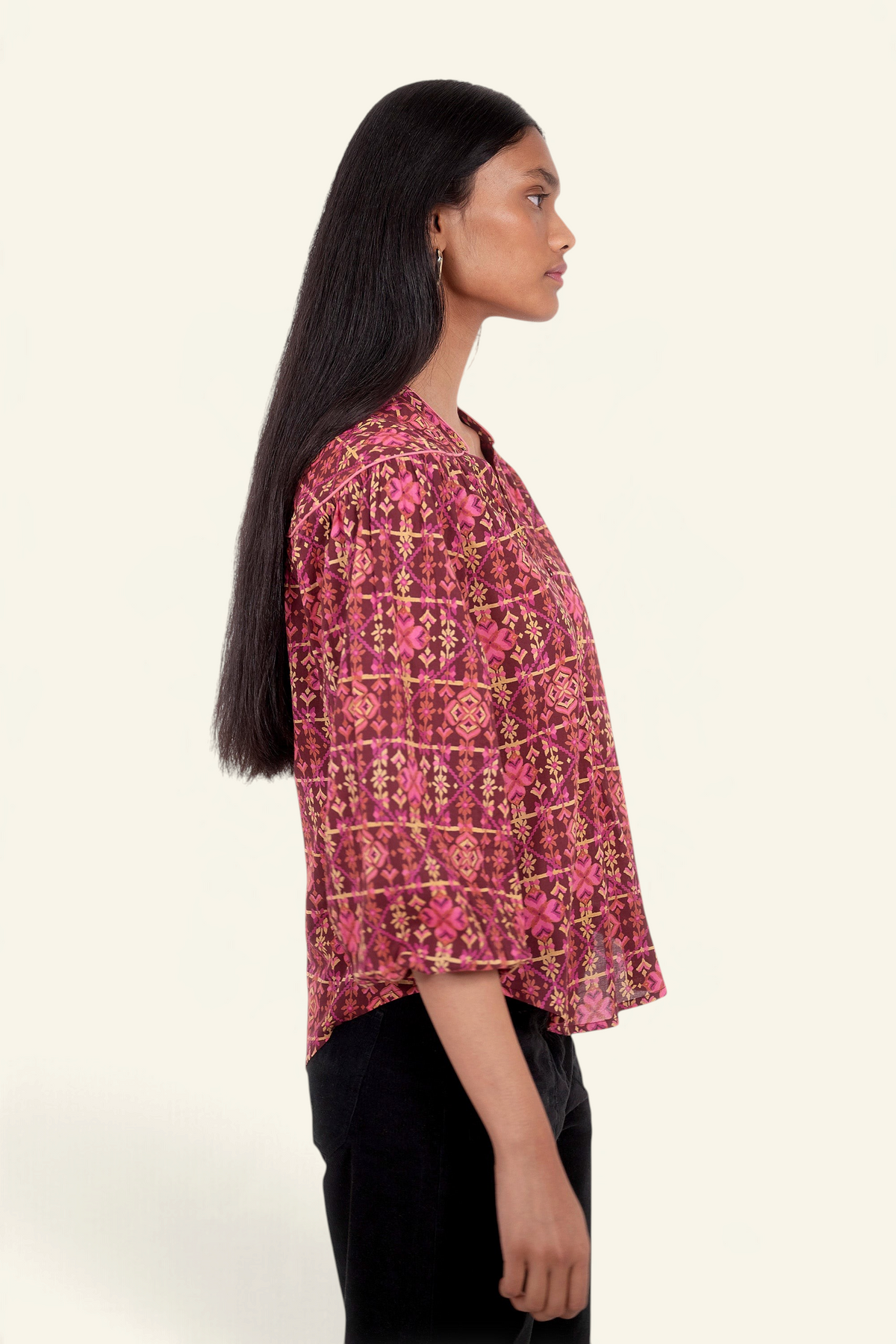 Side view of model standing. She is wearing Banjanan Vanessa top in mahogany cotton voile with a pink geometric floral needlepoint print and v-neckline.