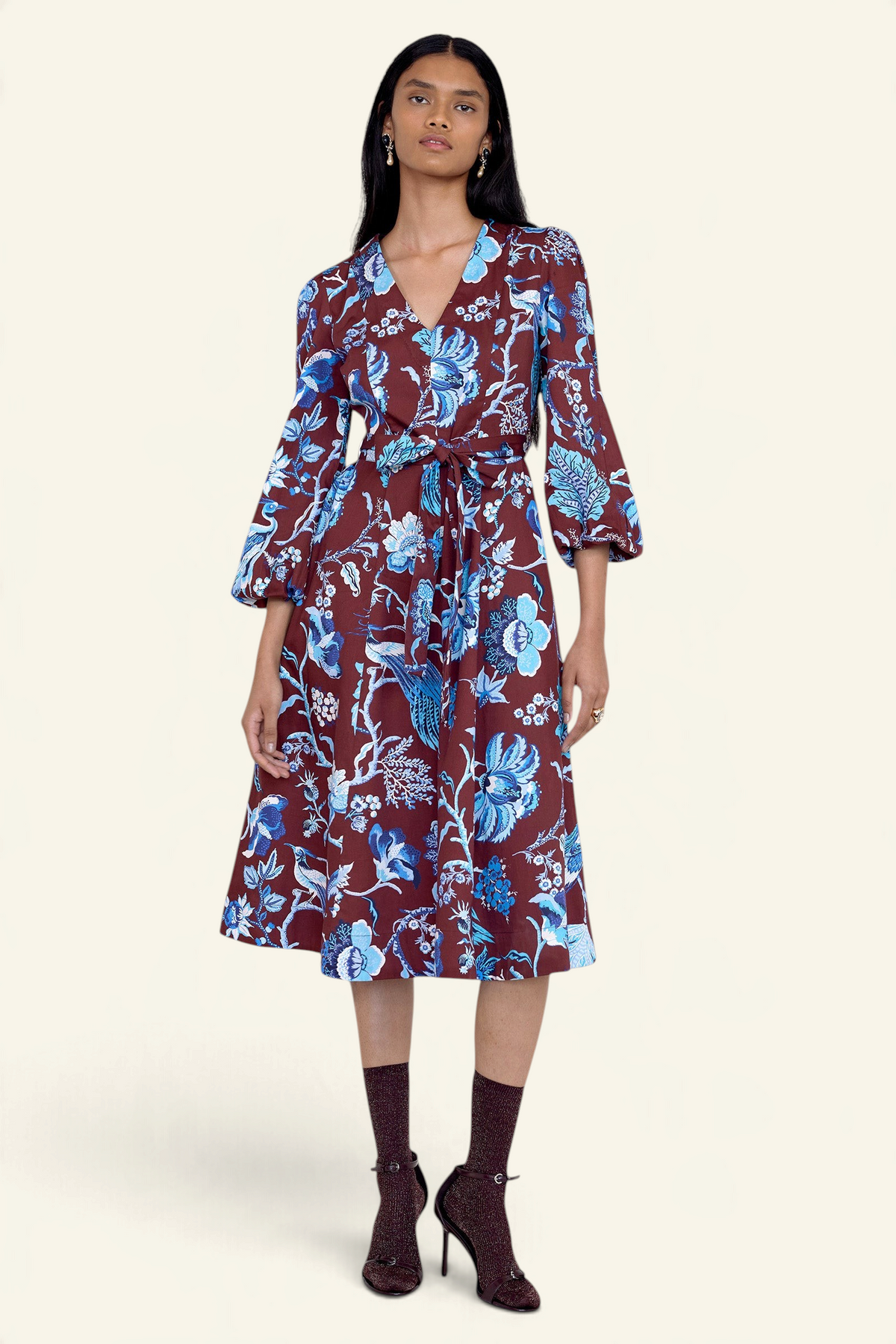 Front view of model standing. She is wearing the Zora dress in Chintz print, featuring a V-neck, lantern sleeves, princess seams, a gathered fit-and-flare skirt, fabric belt, and side-seam pockets.