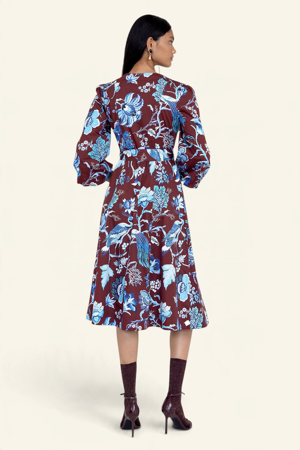 Back view of model standing. She is wearing the Zora dress in Chintz print, featuring a V-neck, lantern sleeves, princess seams, a gathered fit-and-flare skirt, fabric belt, and side-seam pockets.
