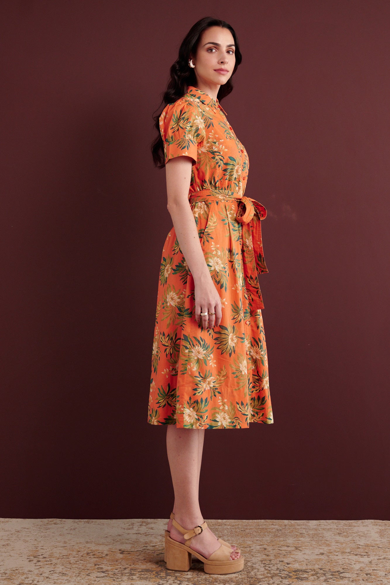 Side view of woman standing. She is wearing the Barbara day dress in Artichoke Flower print. It has gathered sleeves, chest pockets, fabric belt, button details, and a subtly structured yet romantic silhouette.