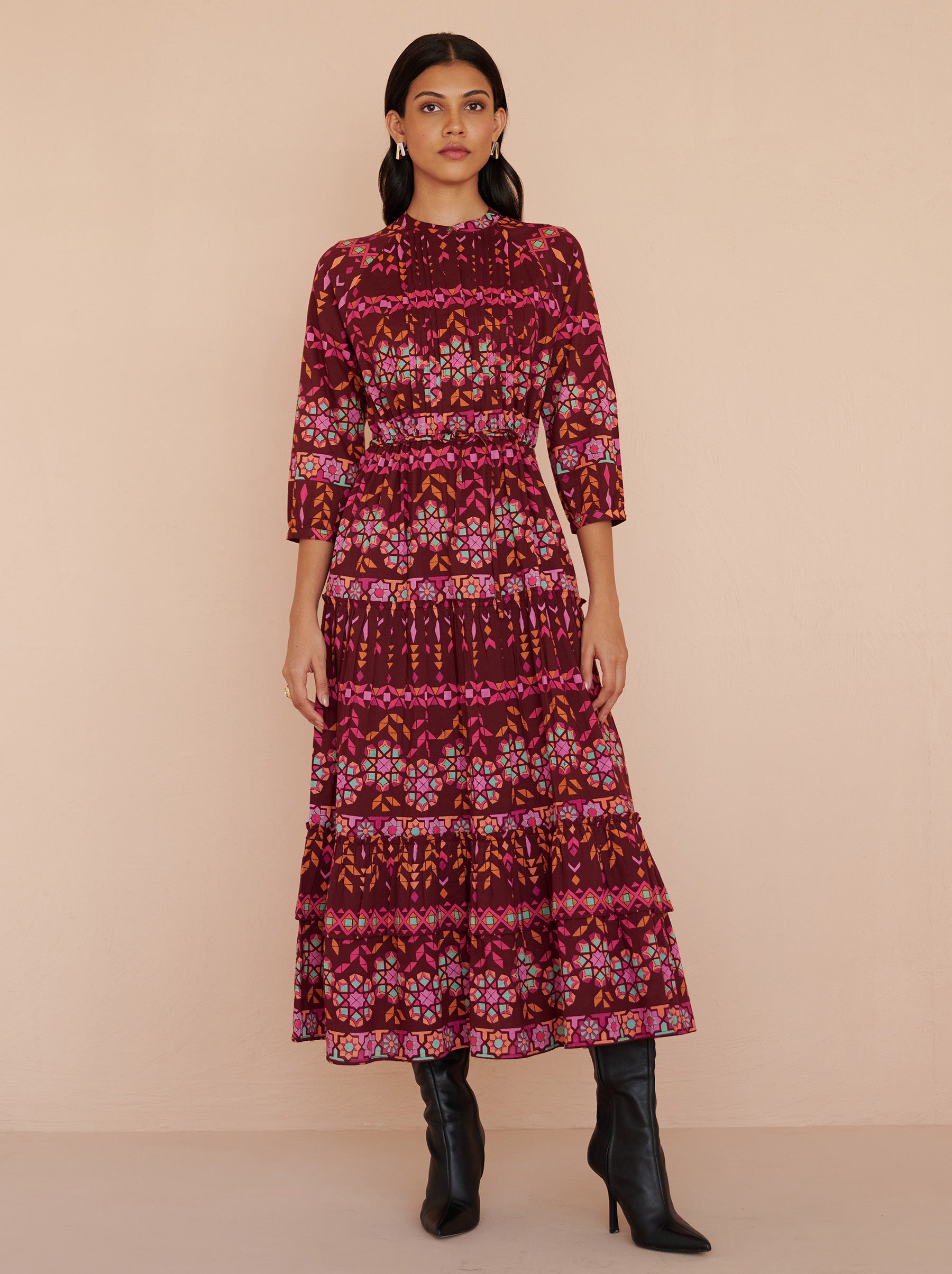 Front view of a model standing. She is wearing the Bazaar ankle-length dress in cotton voile with the Tapestry print in Rhubarb color. It is featuring long sleeves, a tiered A-line skirt, a drawstring self-belt, full lining, and side-seam pockets.
