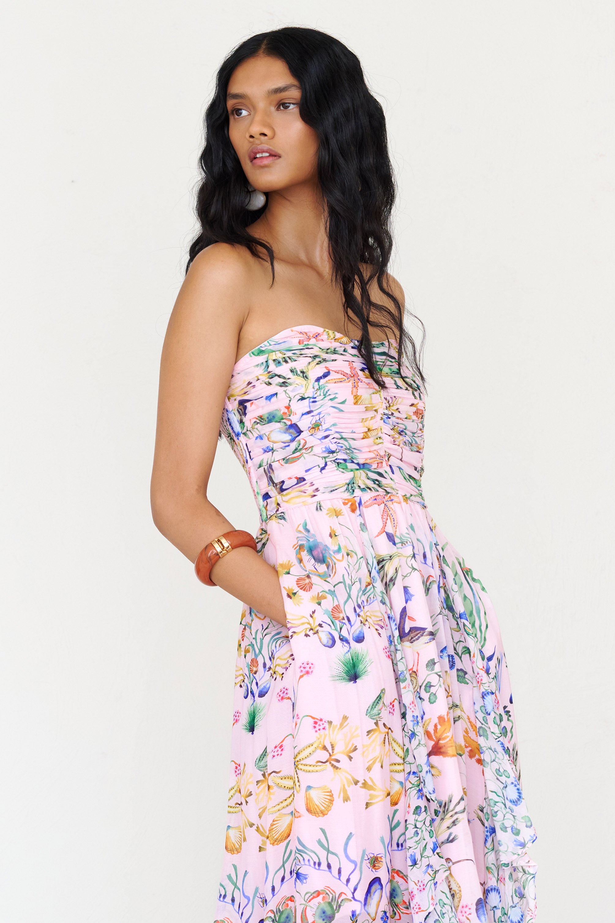 Side view close up of a woman standing wearing the Bella dress in Tidepool print, featuring a full-length cascading skirt with contrast frill, ruched bodice, smocked back, side-seam pockets, and drapey viscose voile.