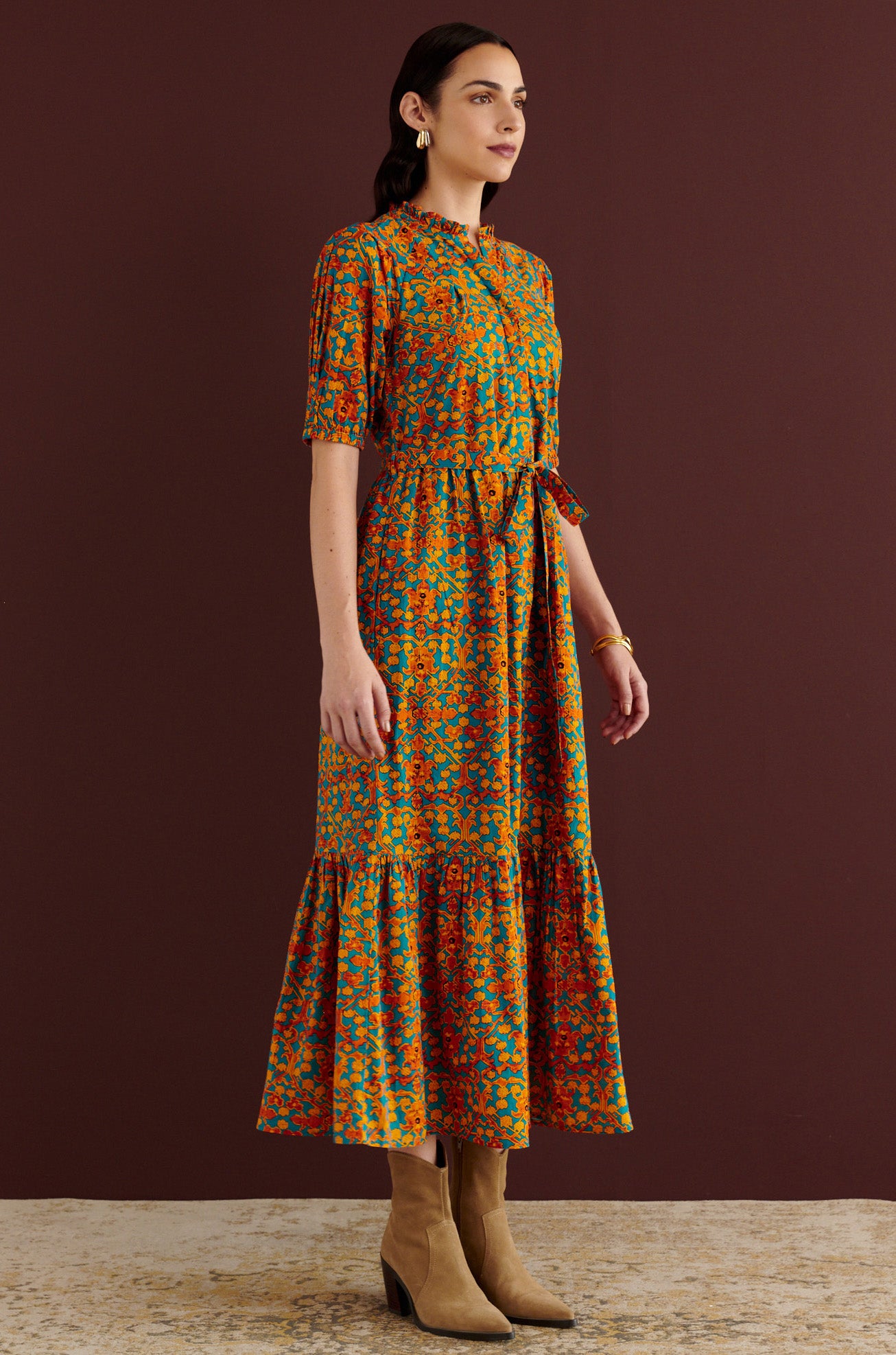 Side view of woman standing. She is wearing the Betty dress in Ottoman print. It has nipped waist, full gathered skirt, tucked raglan sleeves, cotton voile fabric, fabric tie belt, fully lined construction, and side-seam pockets.