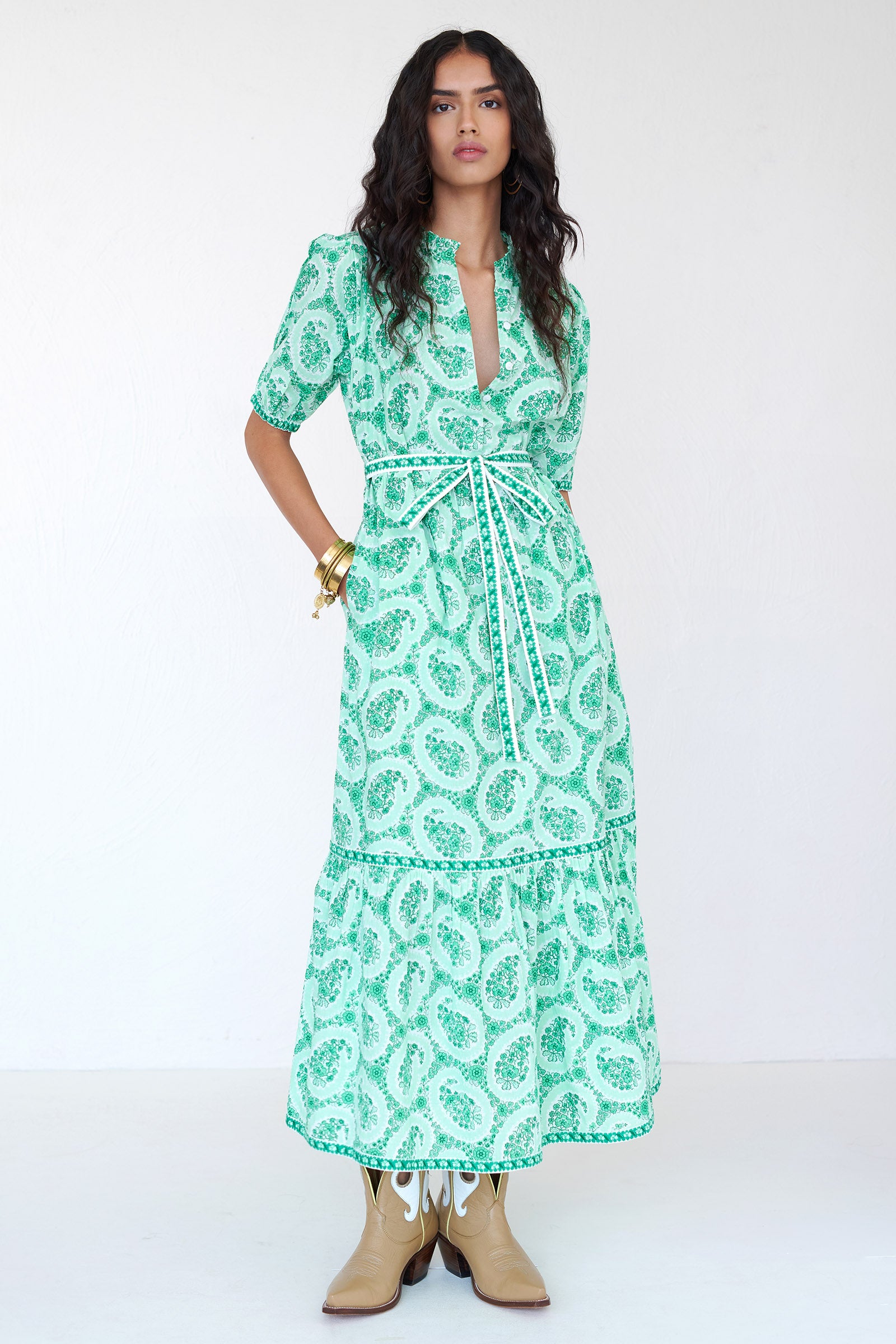 Front view of a woman standing wearing the Betty dress in Paisley Copse print. It features gathered skirt, raglan sleeves, contrast trim, fabric tie belt, and side-seam pockets in breezy cotton voile.