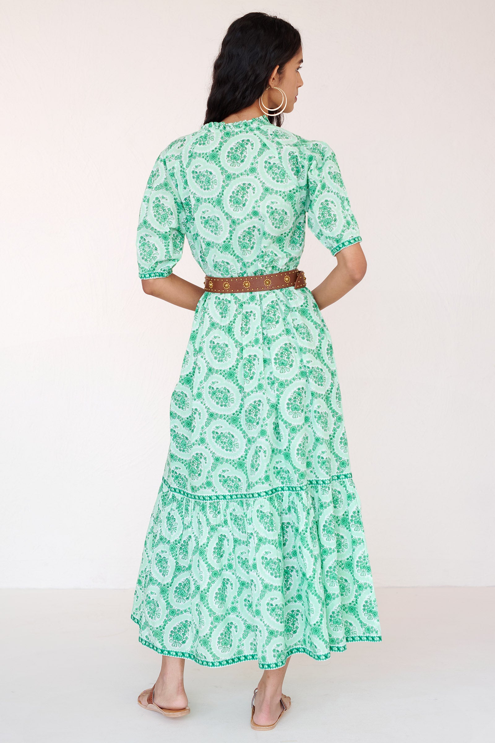 Back view of a woman standing wearing the Betty dress in Paisley Copse print. It features gathered skirt, raglan sleeves, contrast trim and side-seam pockets in breezy cotton voile. Styled with brown belt.