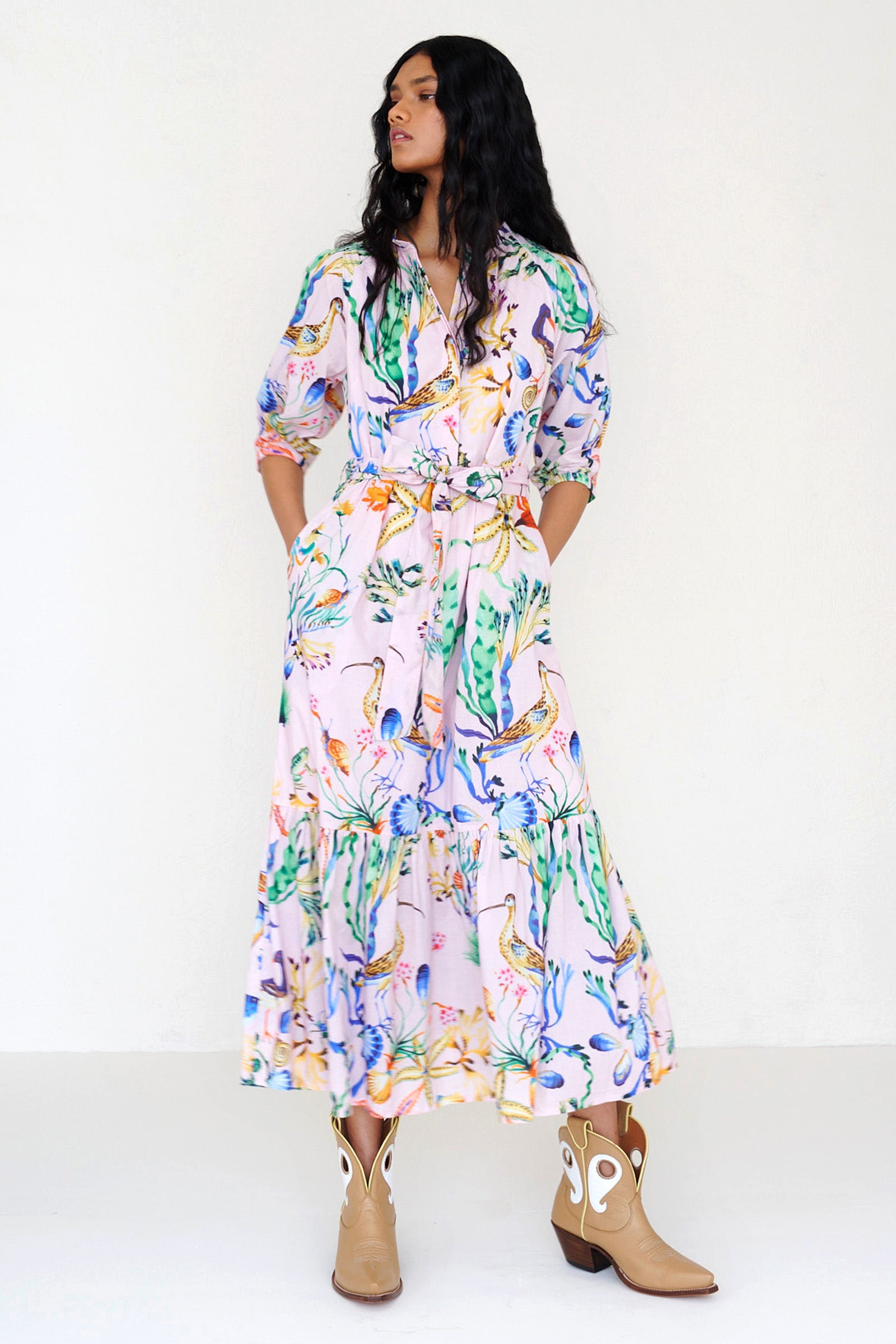 Front view of a woman standing. She is wearing the Betty dress in Tidepool print. It features a nipped waist, voluminous gathered skirt, tucked raglan sleeves, fabric tie belt & pockets.