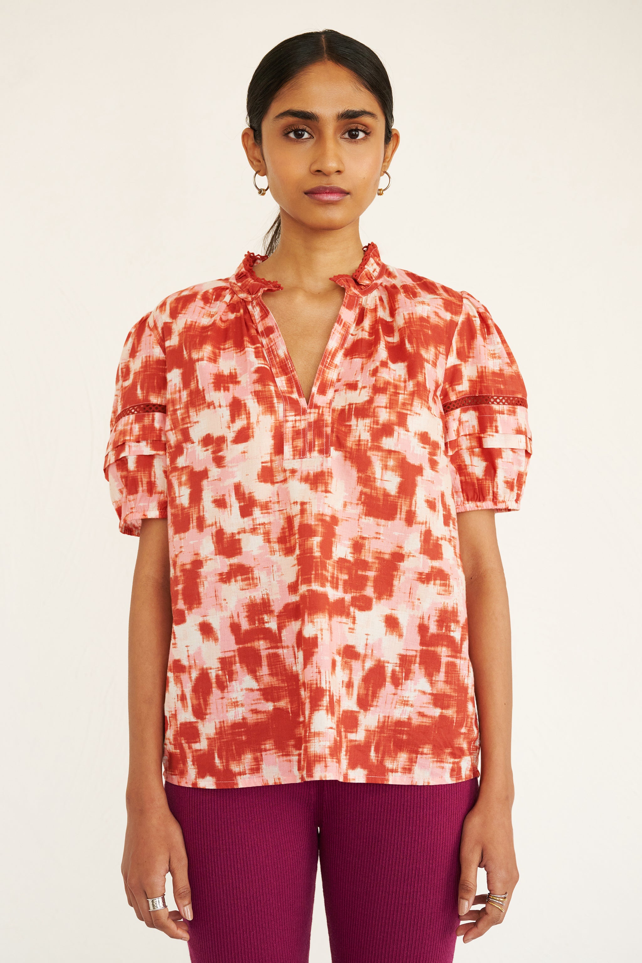 Front view of woman wearing a cotton top with an ikat-inspired print, lace sleeve insets, a split neckline, and pleated sleeves.