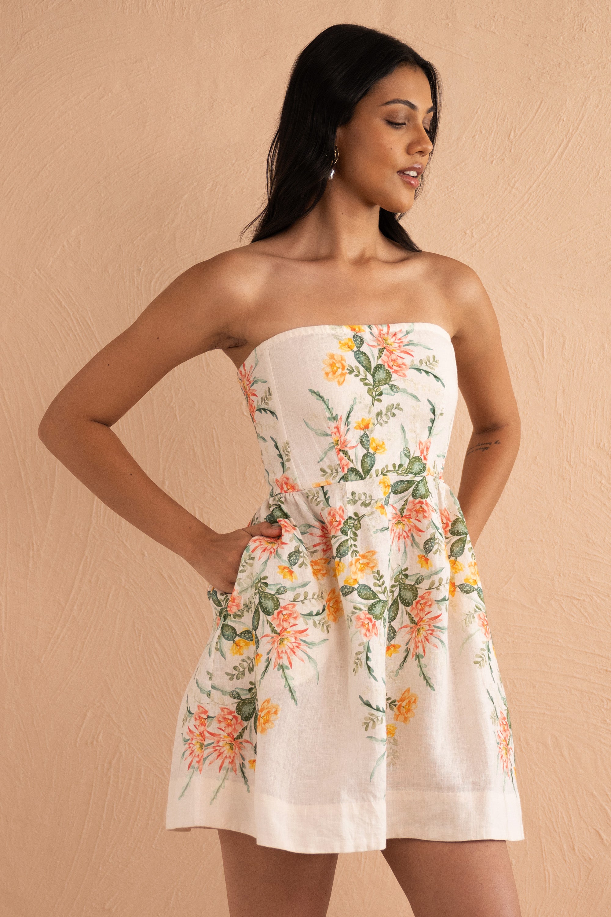 Front view close up of woman wearing strapless Simona Mini Dress in Desert Rose Dawn print, featuring boned bodice, gathered mini skirt, side-seam pockets, and back zipper in linen with watercolor cactus flowers.