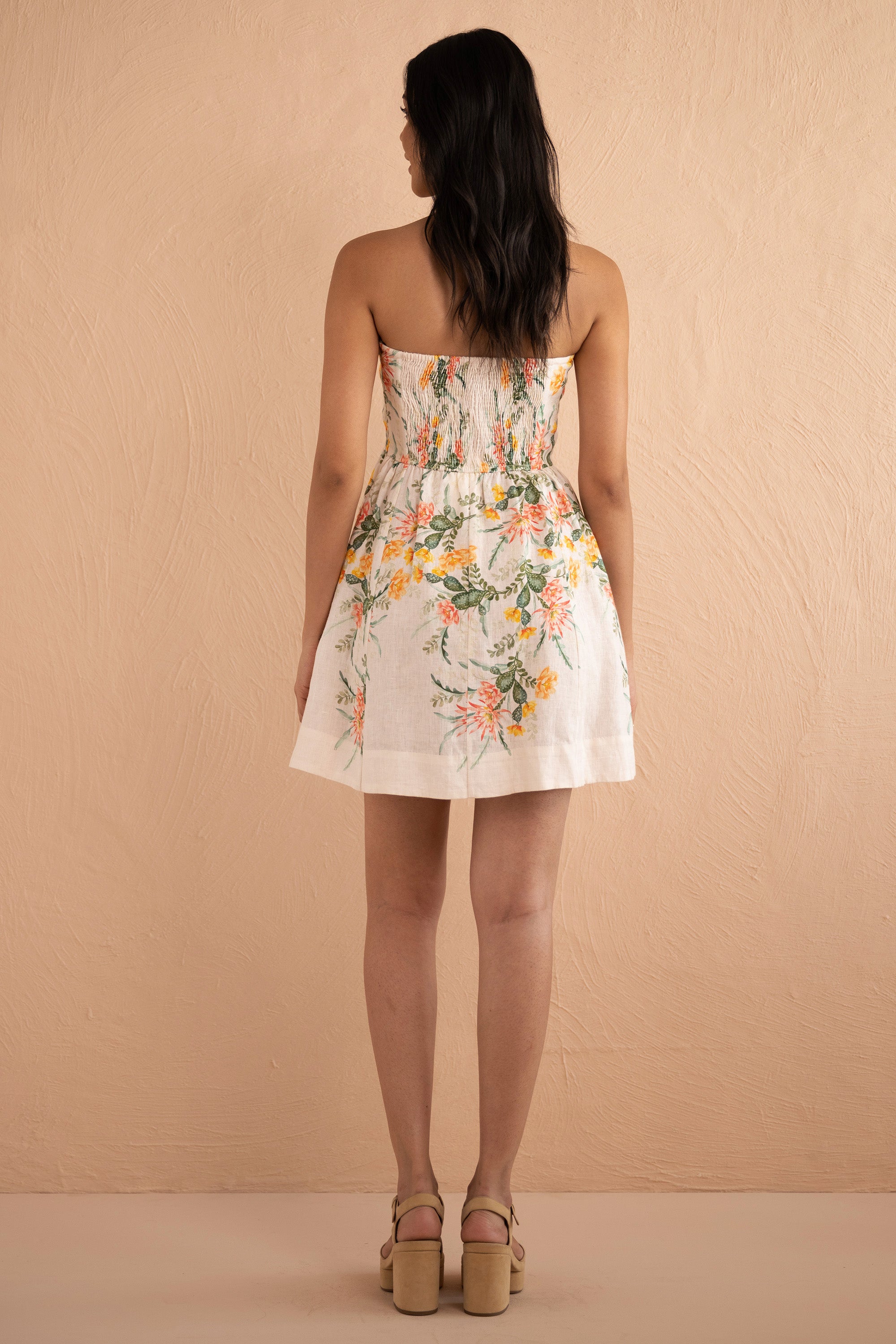 Back view of woman wearing strapless Simona Mini Dress in Desert Rose Dawn print, featuring boned bodice, gathered mini skirt, side-seam pockets, and back zipper in linen with watercolor cactus flowers.