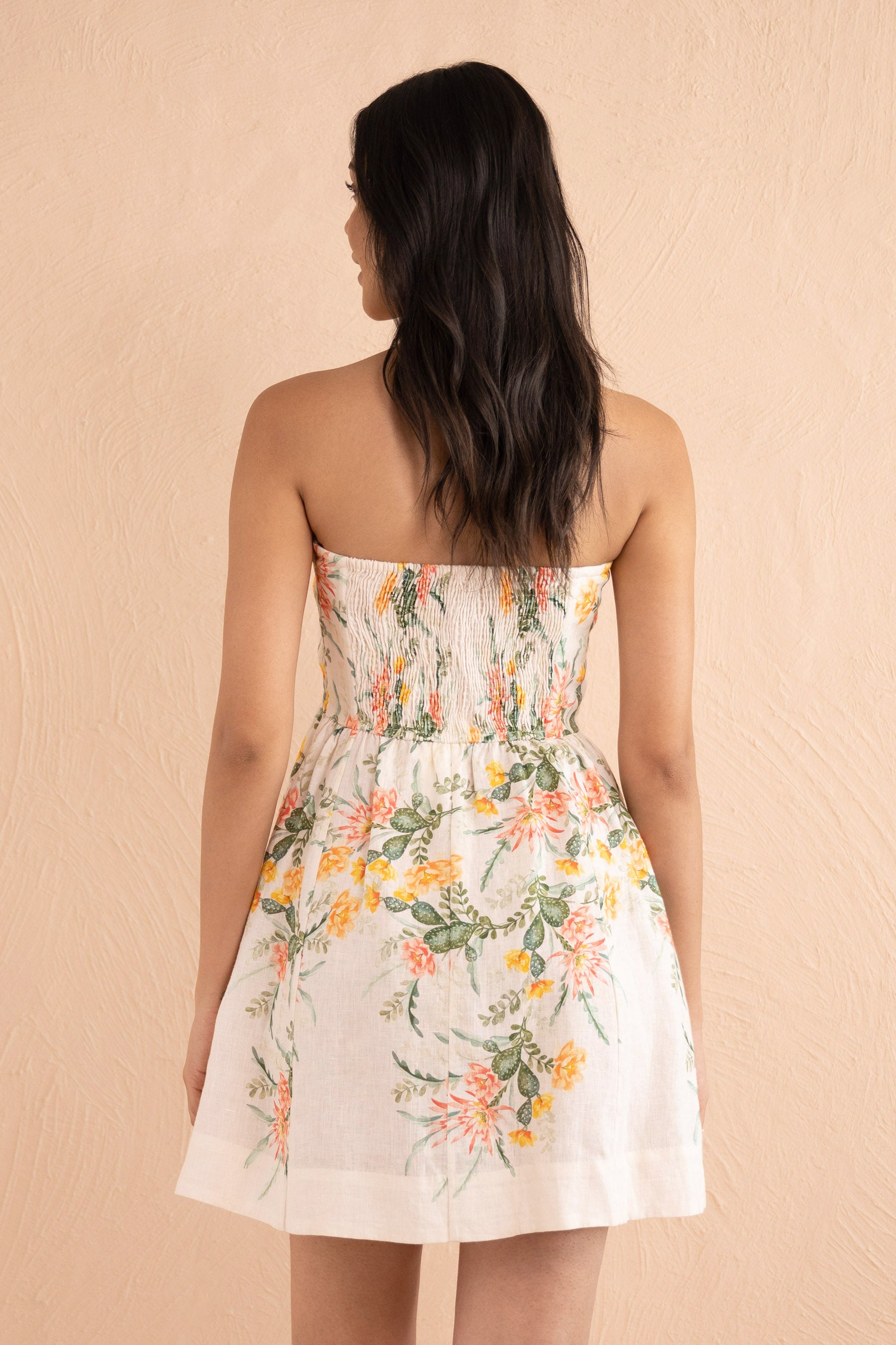 Back view close up of model posing wearing a strapless mini dress, the Simona Dress in Desert Rose Dawn print in linen.