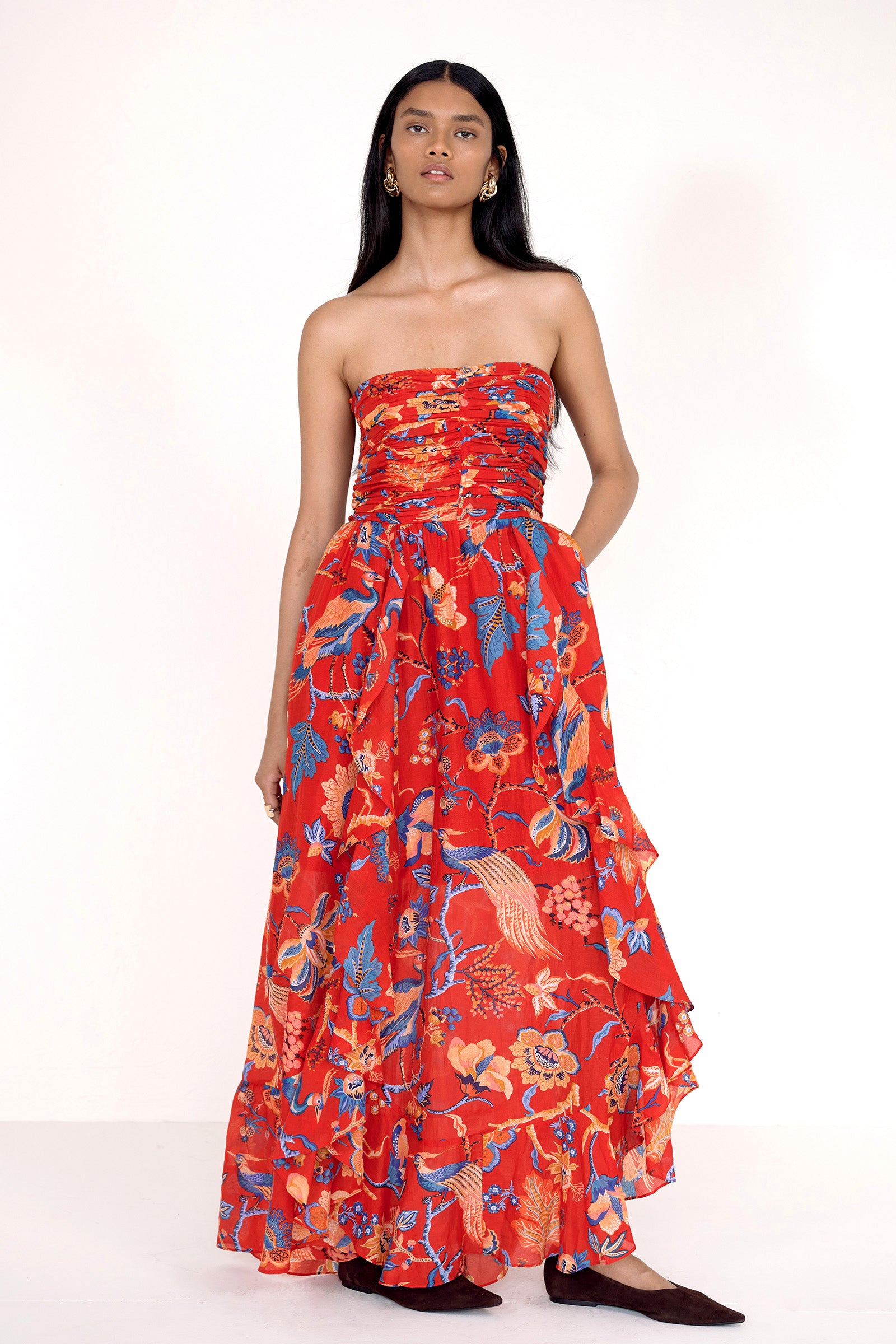 Front view of model standing. She is wearing the Bella dress in Chintz print with left hand in pocket. It features a full-length cascading skirt, subtle frill detail, ruched bodice, and smocked back.