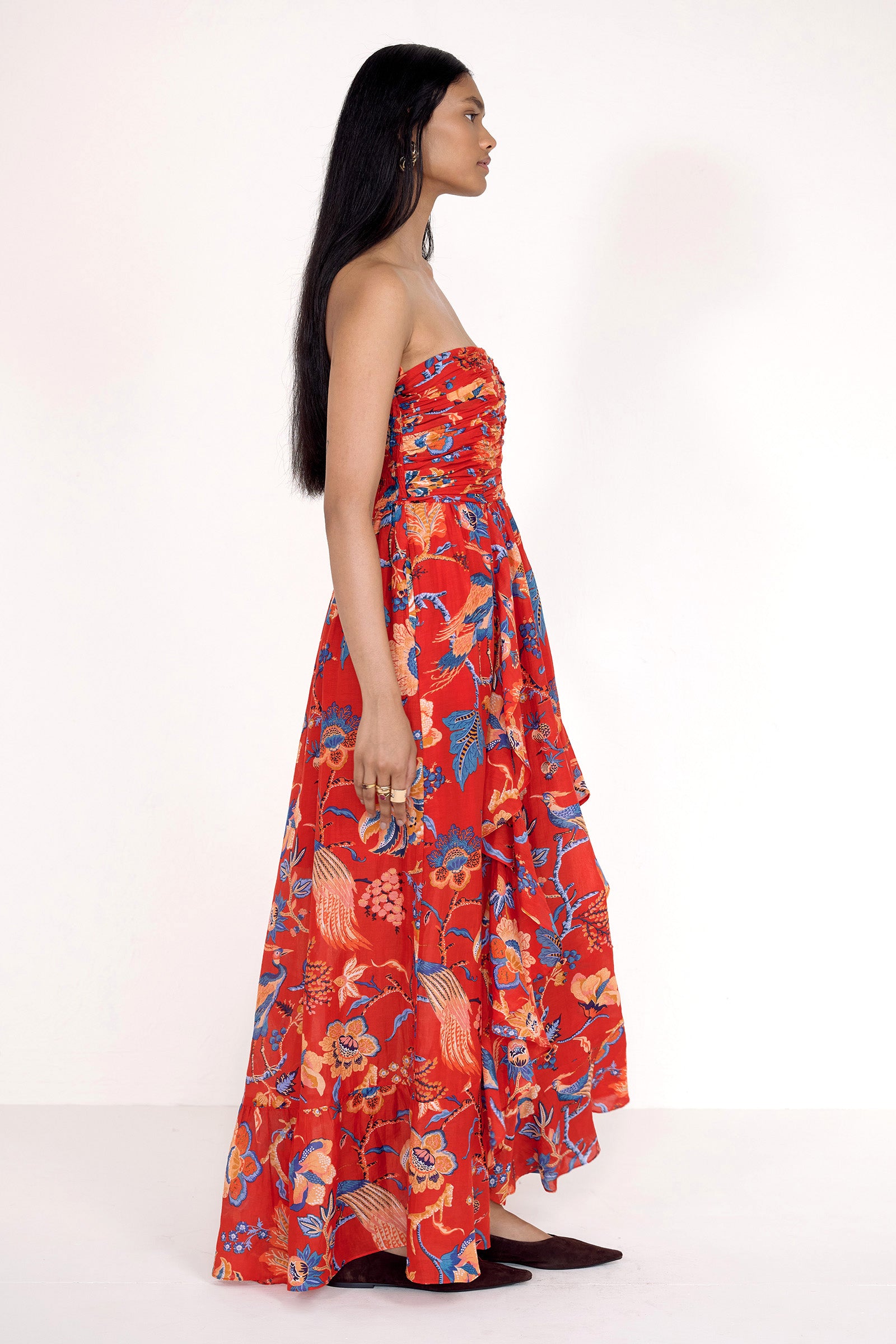 Side view of model standing. She is wearing the Bella dress in Chintz print. It features a full-length cascading skirt, subtle frill detail, ruched bodice, and smocked back.