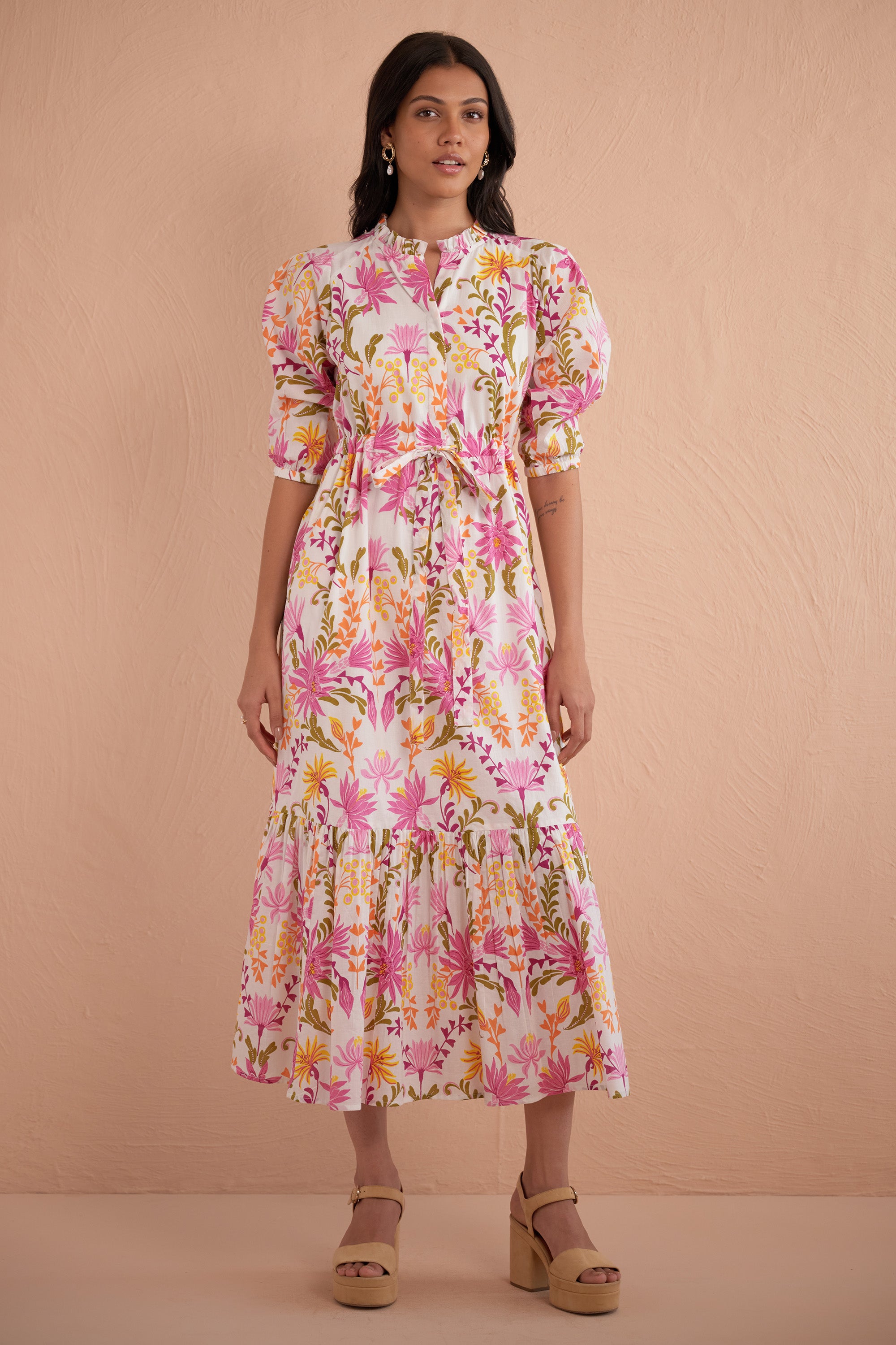 Front view of woman wearing Betty Dress in Hydra Garland Rose print, featuring a cinched waist, full gathered skirt, tucked raglan sleeves, concealed front button placket, drawstring waist, and side-seam pockets in bold sunset floral cotton voile.