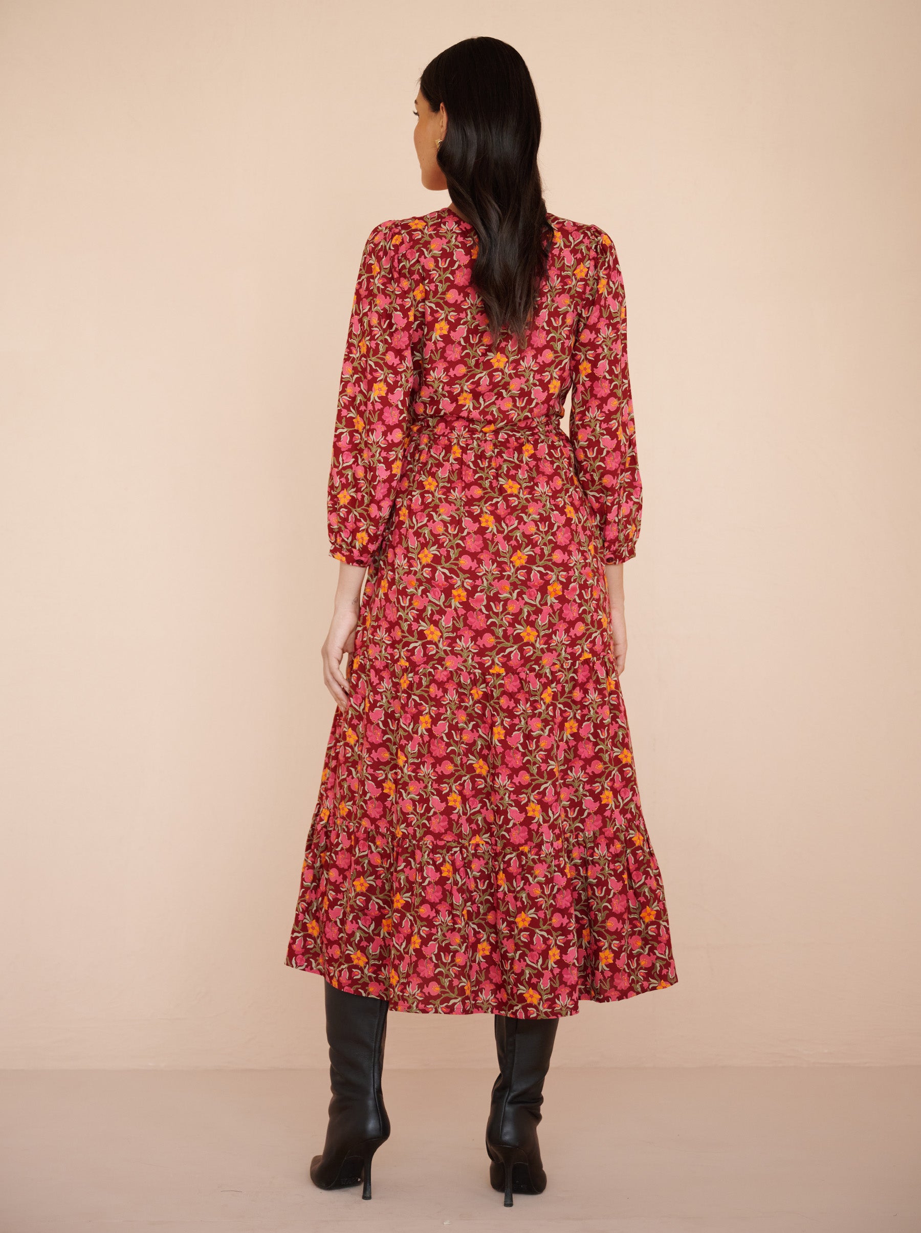 Back view of a model standing. She is wearing the Castor dress in eco-friendly viscose. It is featuring soft puff sleeves, a gathered drawstring skirt to the shin, and the Pomegranate Vine print in Azalea color. The dress is fully lined with side-seam pockets.