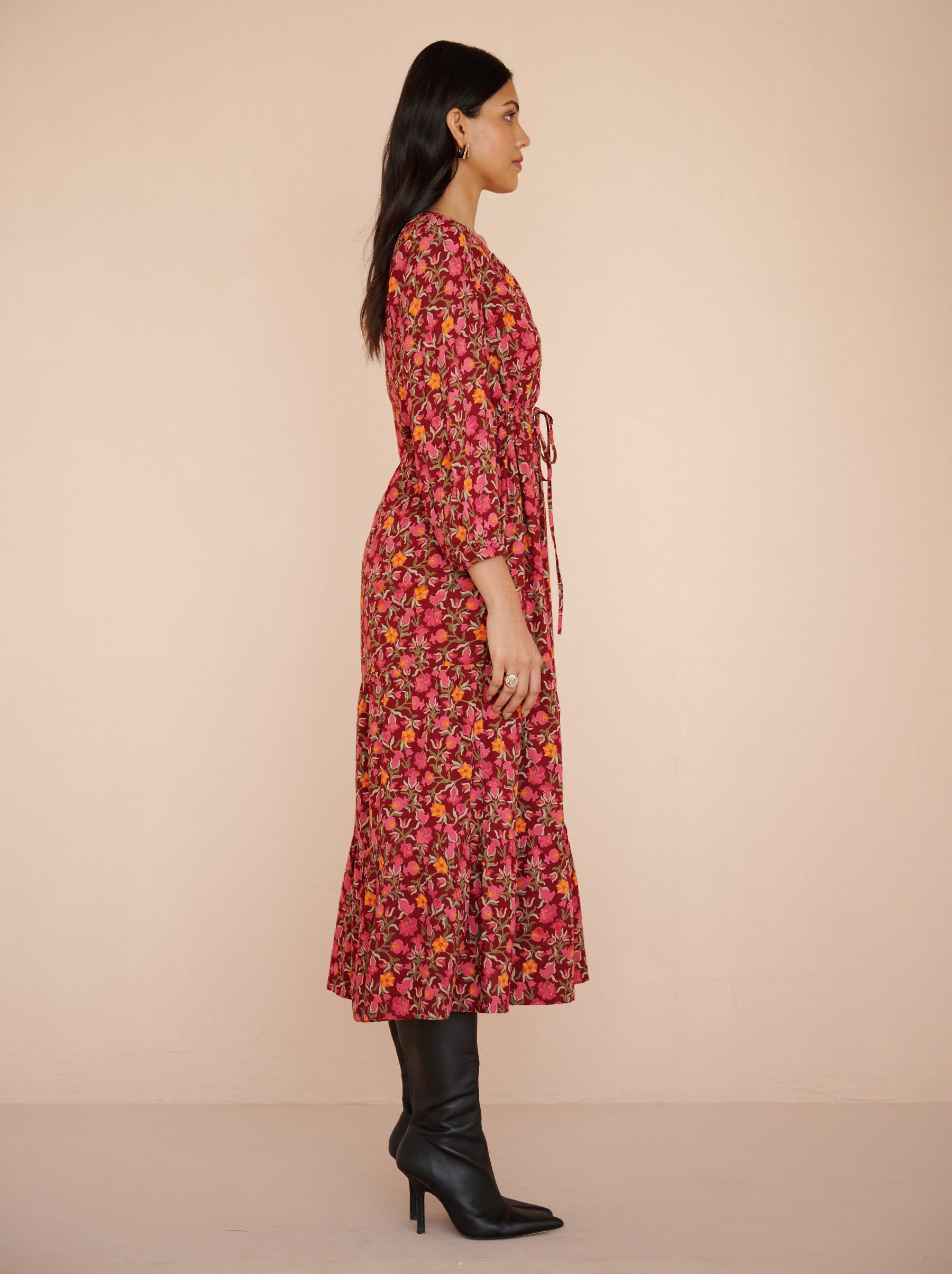 Side view of a model standing. She is wearing the Castor dress in eco-friendly viscose. It is featuring soft puff sleeves, a gathered drawstring skirt to the shin, and the Pomegranate Vine print in Azalea color. The dress is fully lined with side-seam pockets.
