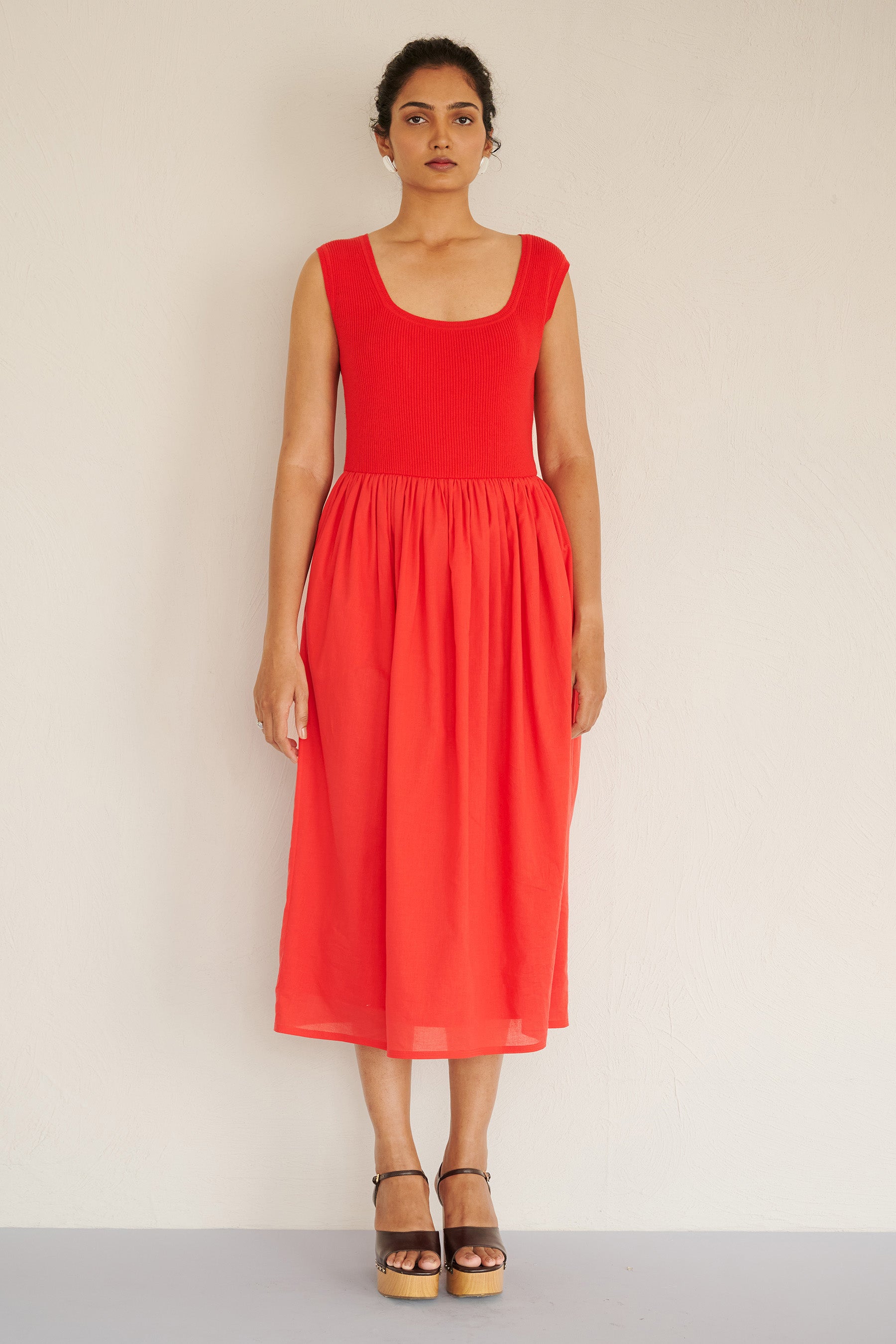 Front view of woman wearing the Chloe dress in poppy red, featuring a ribbed square-neck knit bodice and a tonal cotton voile gathered skirt, styled with platform heels.