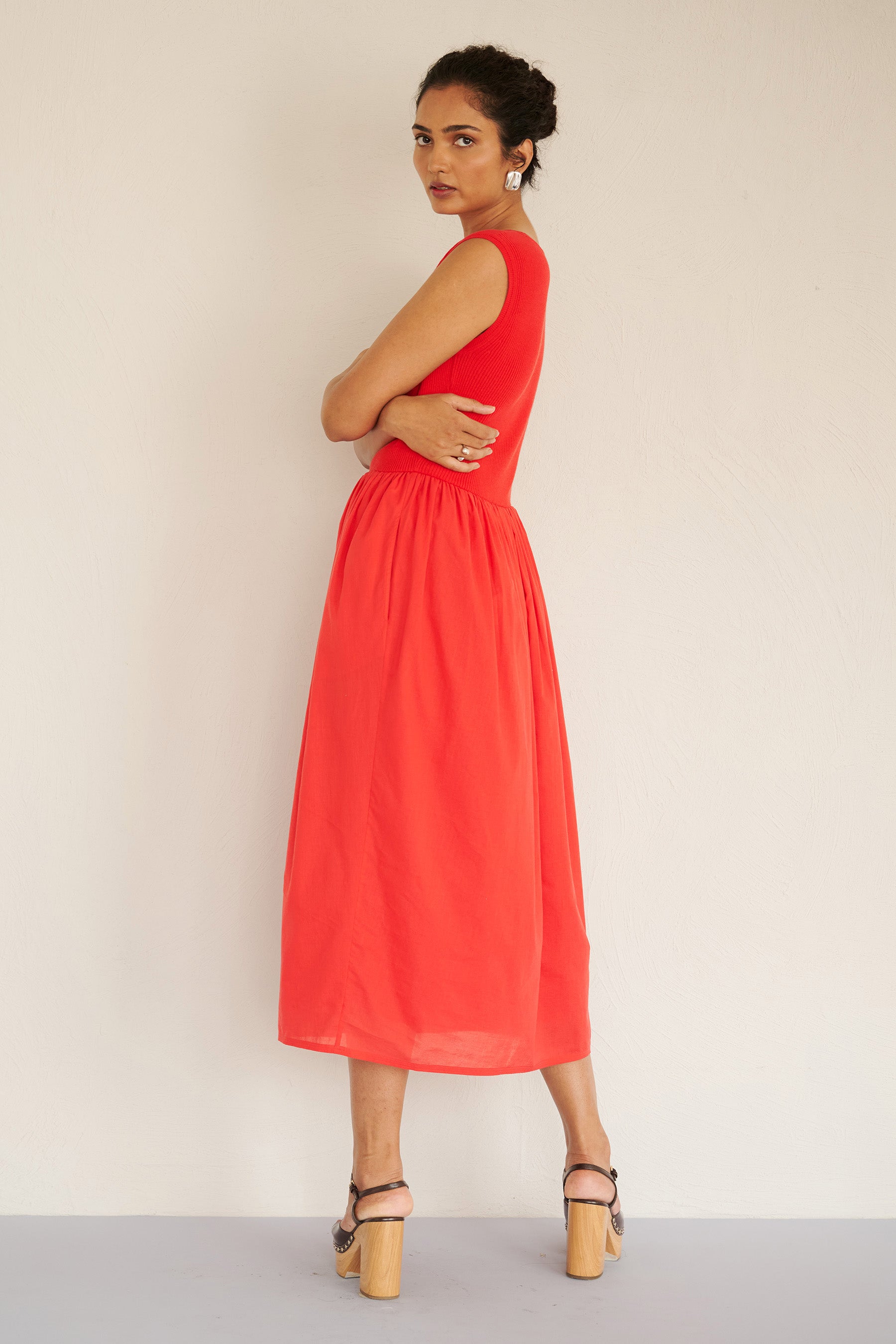 Back view of woman wearing the Chloe dress in poppy red, featuring a ribbed square-neck knit bodice and a tonal cotton voile gathered skirt, styled with platform heels.