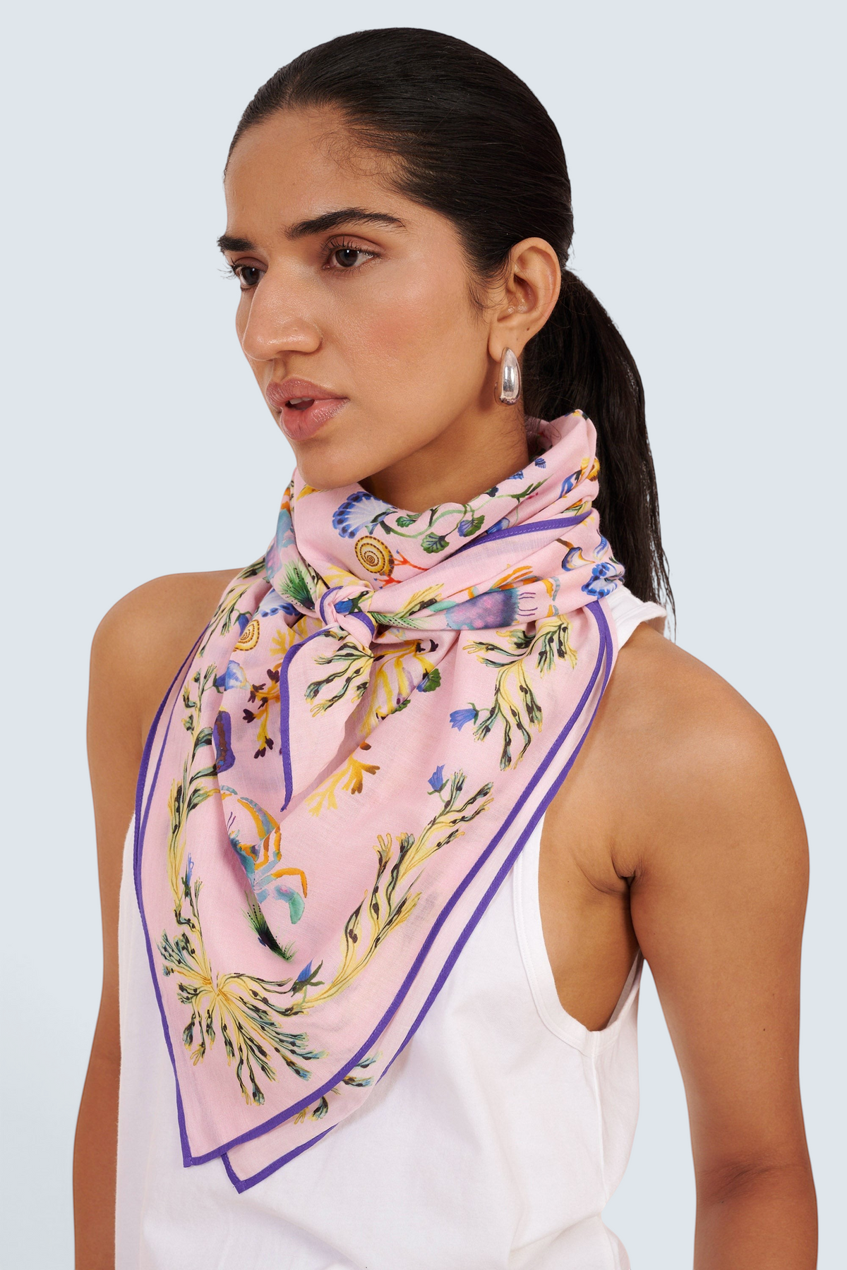 Front side-view close-up of woman standing, wearing the Carolina scarf around her neck in the Tidepool print featuring starfish, seahorse, and shell motifs.
