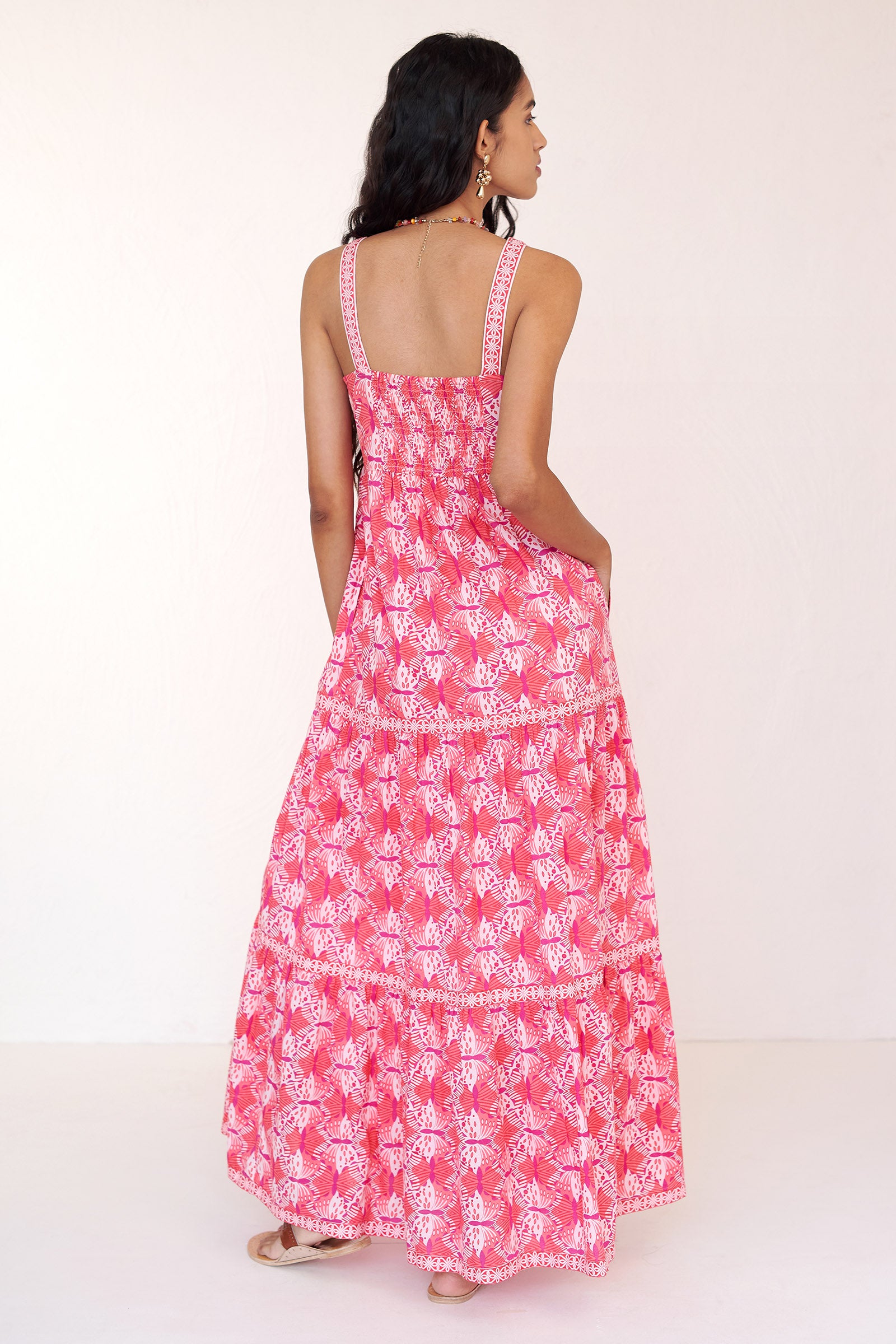Back view of woman wearing the Daniella dress in the Flutter print. It features a flowing cotton voile dress with abstract butterfly motifs and lace trim detailing.