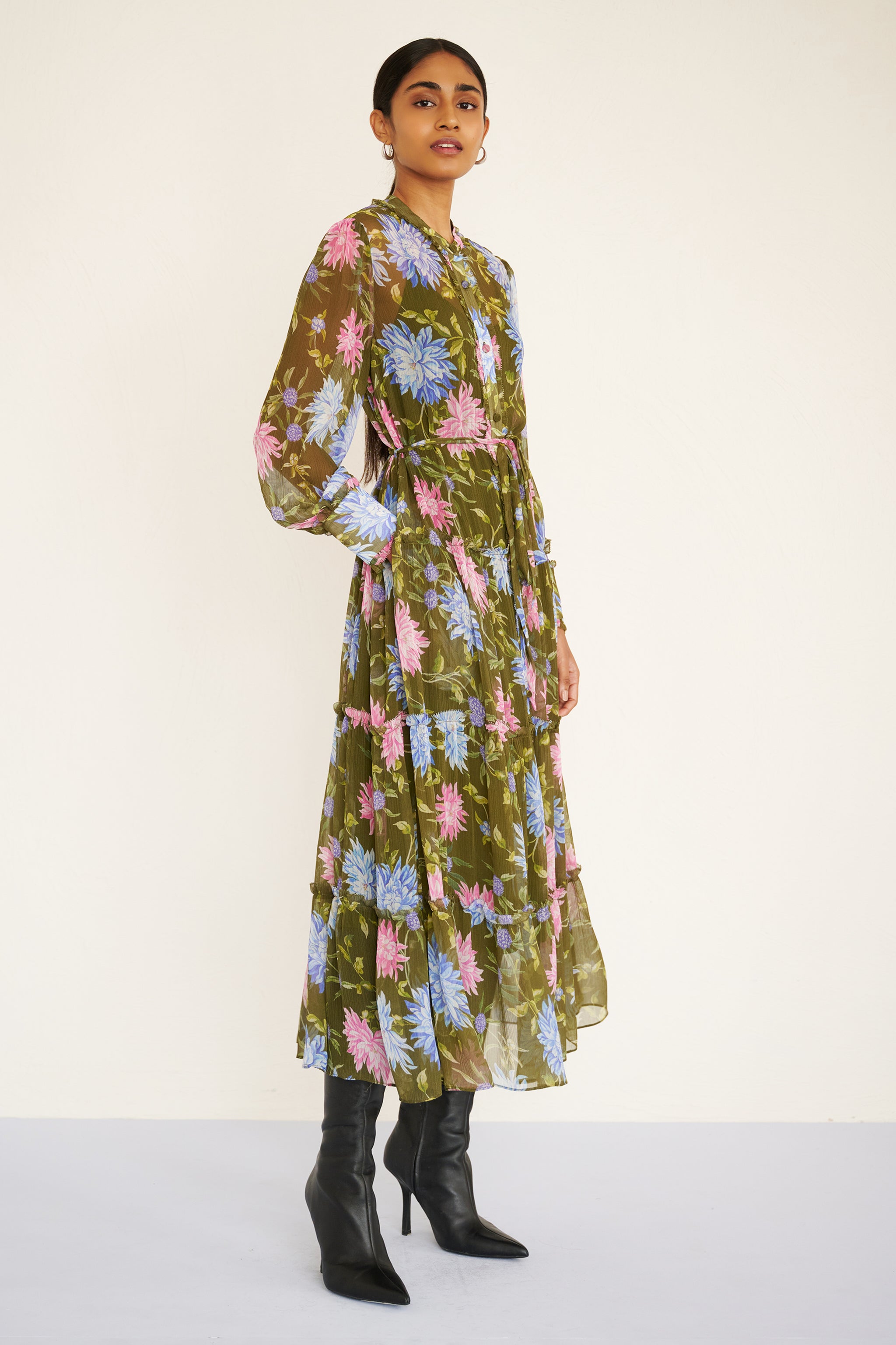 Side view of woman wearing a long-sleeve chiffon midi dress with sheer sleeves, ruffle details, fabric buttons, and a painterly floral print, styled with a detachable belt.