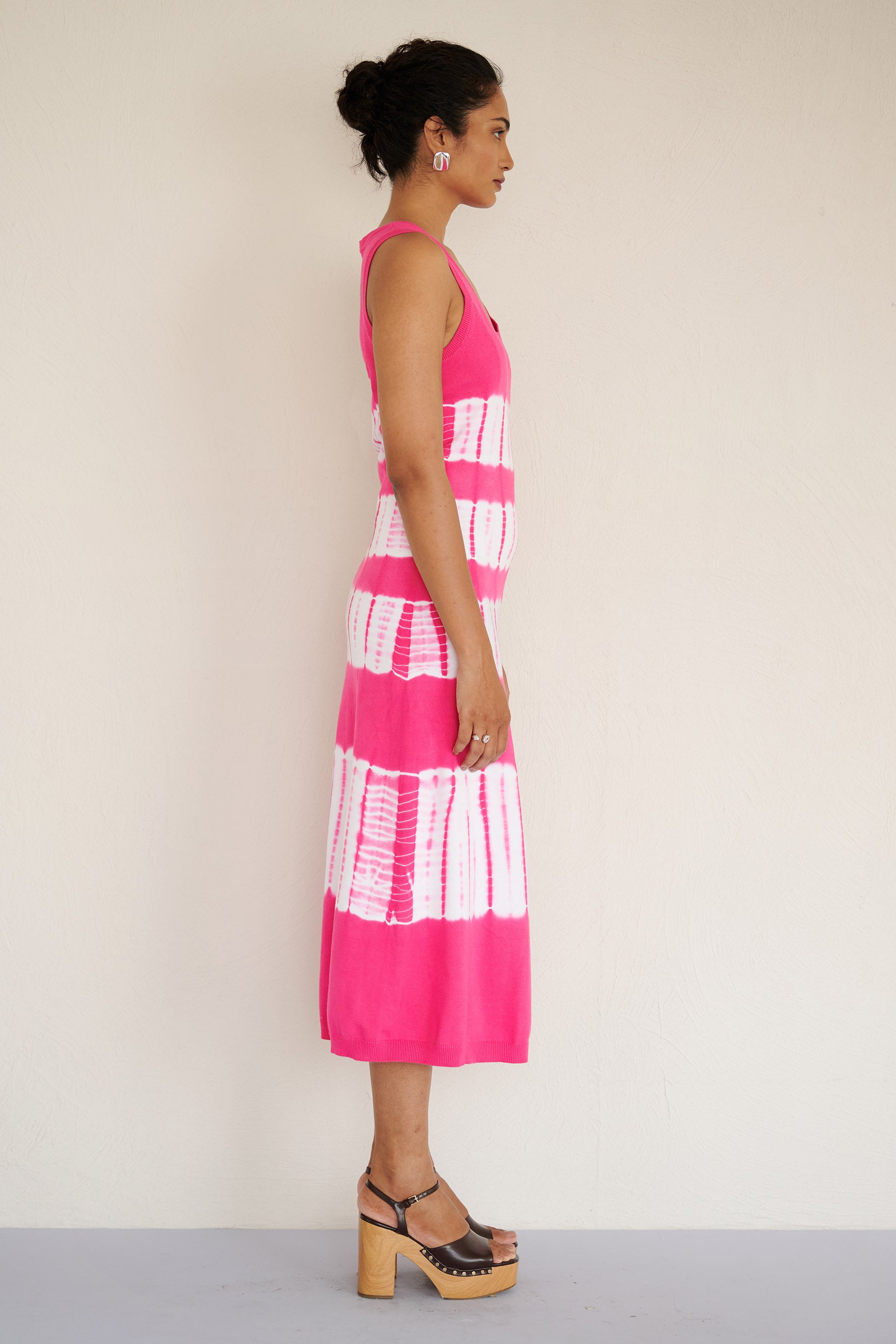 Side view of woman wearing the sleeveless Genoa dress in bold fuchsia pink tie-dye, featuring a body-skimming silhouette with ribbed trims, handcrafted for a one-of-a-kind look.