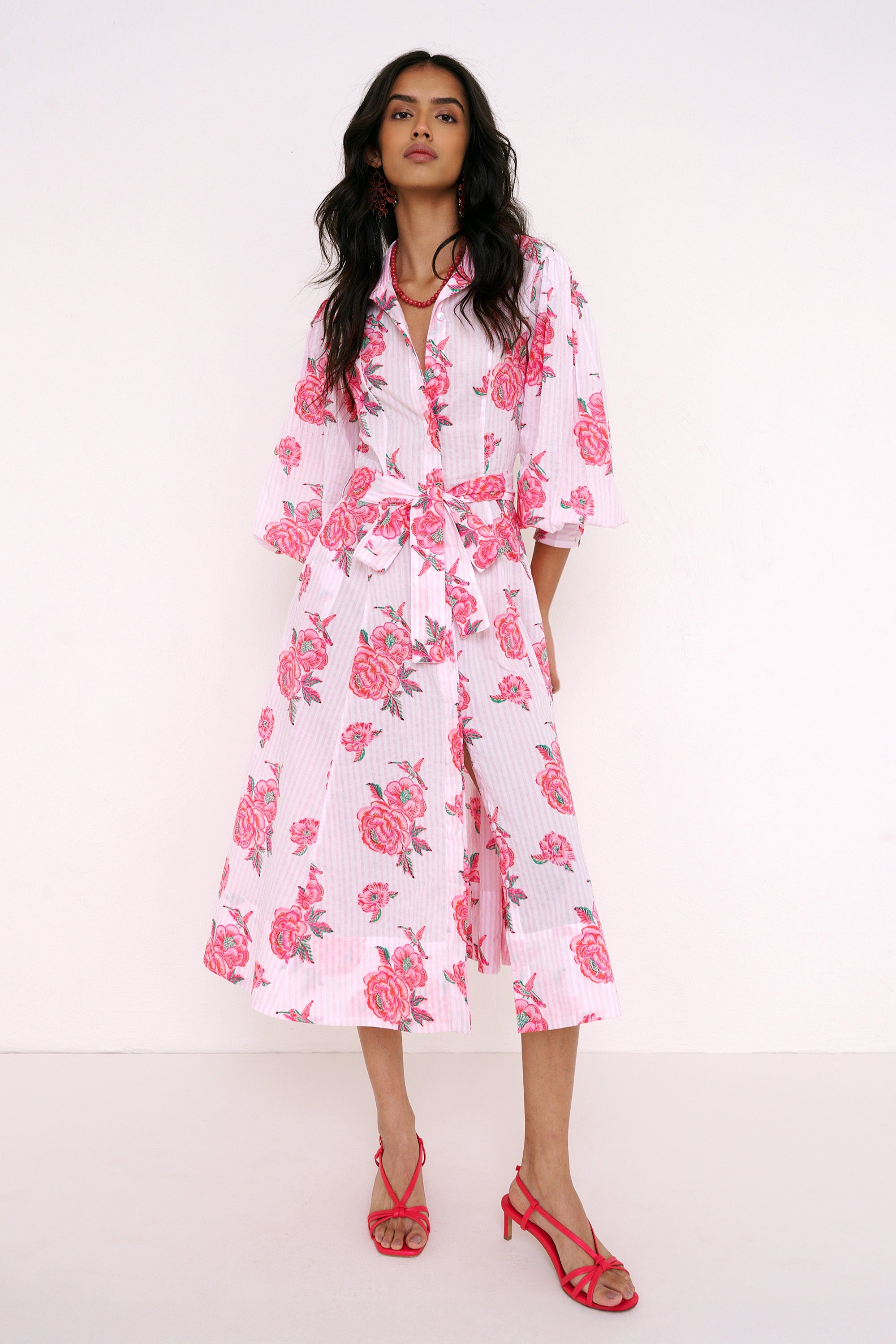 Front view of woman standing . She is wearing the Harris dress in the Eliza Rose print, featuring a fitted shirtdress silhouette, fabric tie belt, flared skirt with godet panels, and hand block-printed floral motifs.