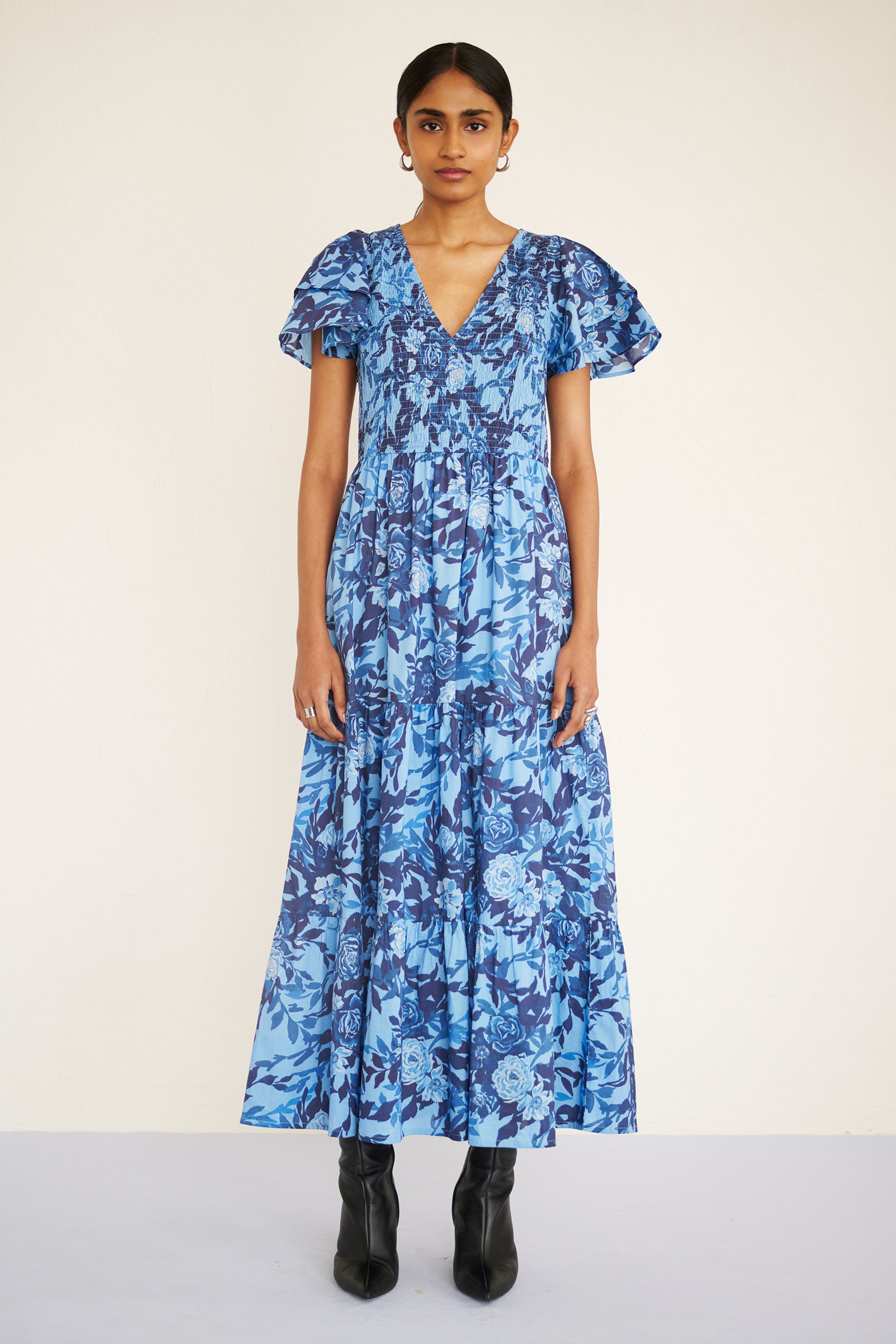 Front view of woman wearing a floral midi dress with smocked bodice, double-ruffled sleeves, and a soft watercolor rose print in tones of blue.