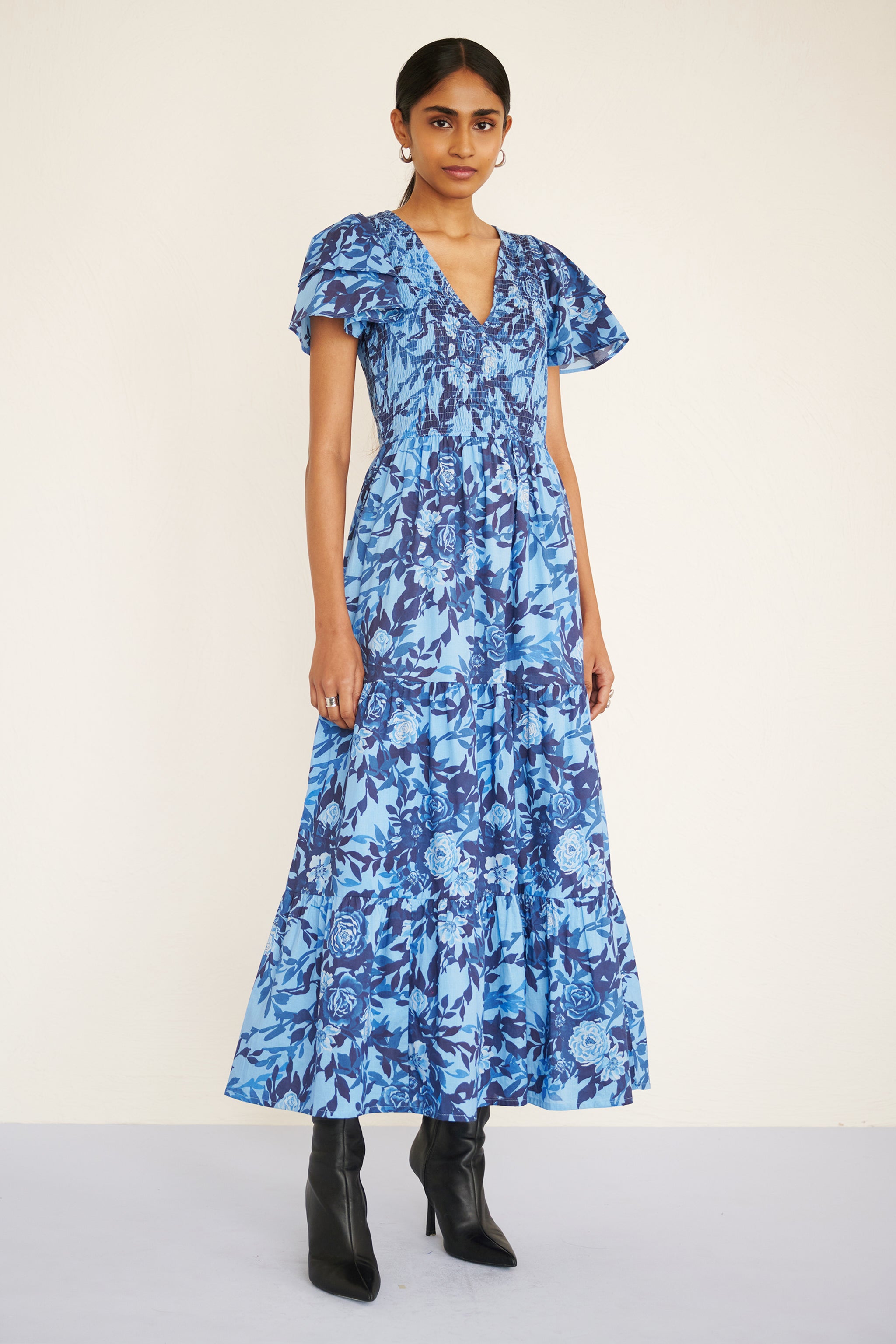 Front view of woman wearing a floral midi dress with smocked bodice, double-ruffled sleeves, and a soft watercolor rose print in tones of blue.