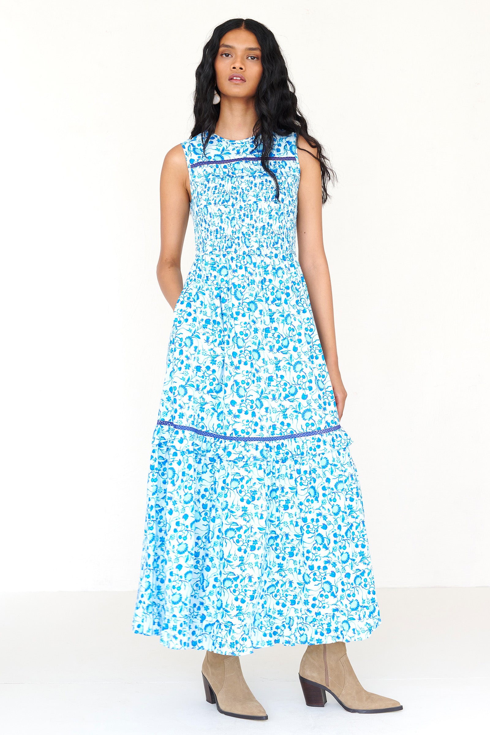 Front view of a woman standing wearing the Iris dress in Clam Garland print. It features a smocked bodice, tonal lace detailing, keyhole back with loop button and pockets.