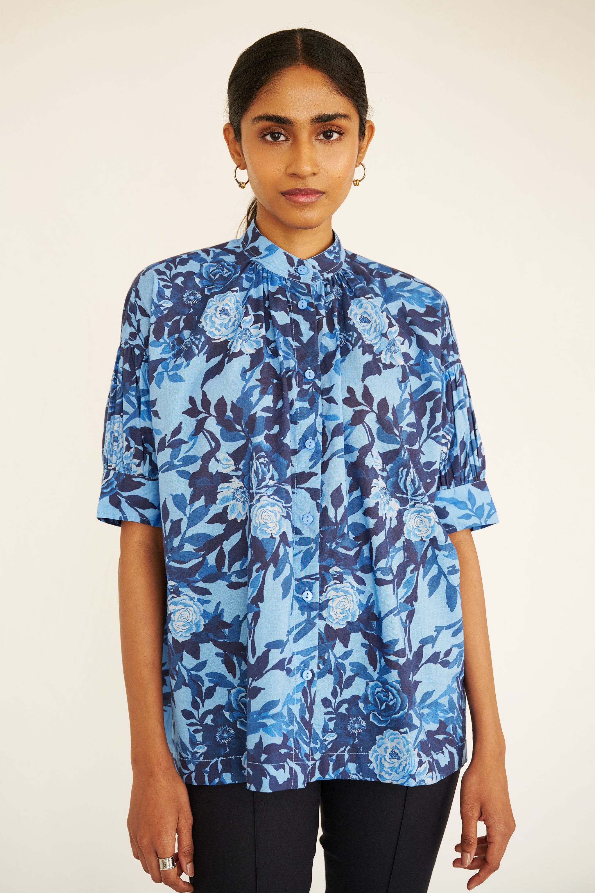 Front view of woman wearing a relaxed floral button-down shirt with drop shoulders, stand collar, and gathered neckline.