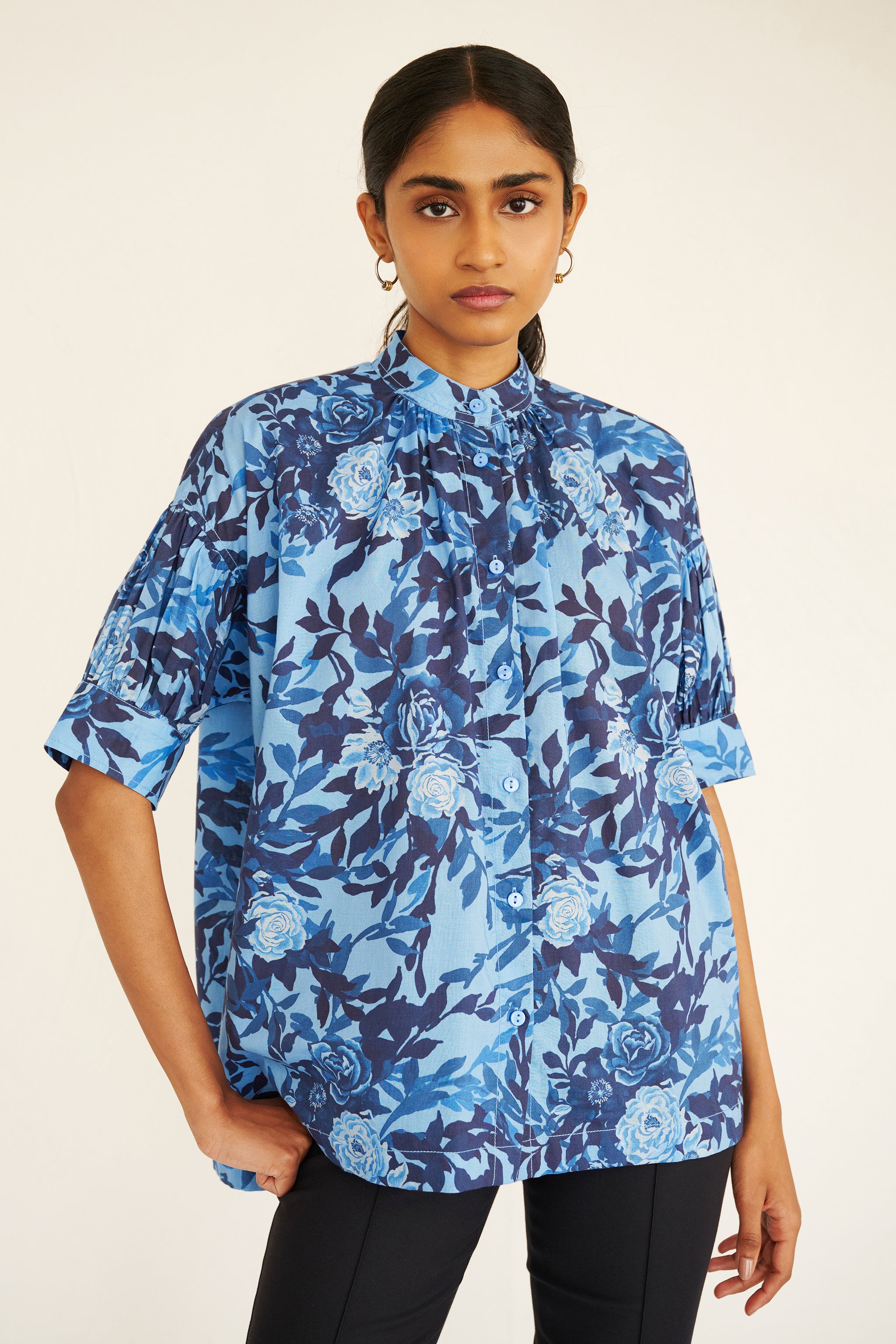 Front view of woman wearing a relaxed floral button-down shirt with drop shoulders, stand collar, and gathered neckline.