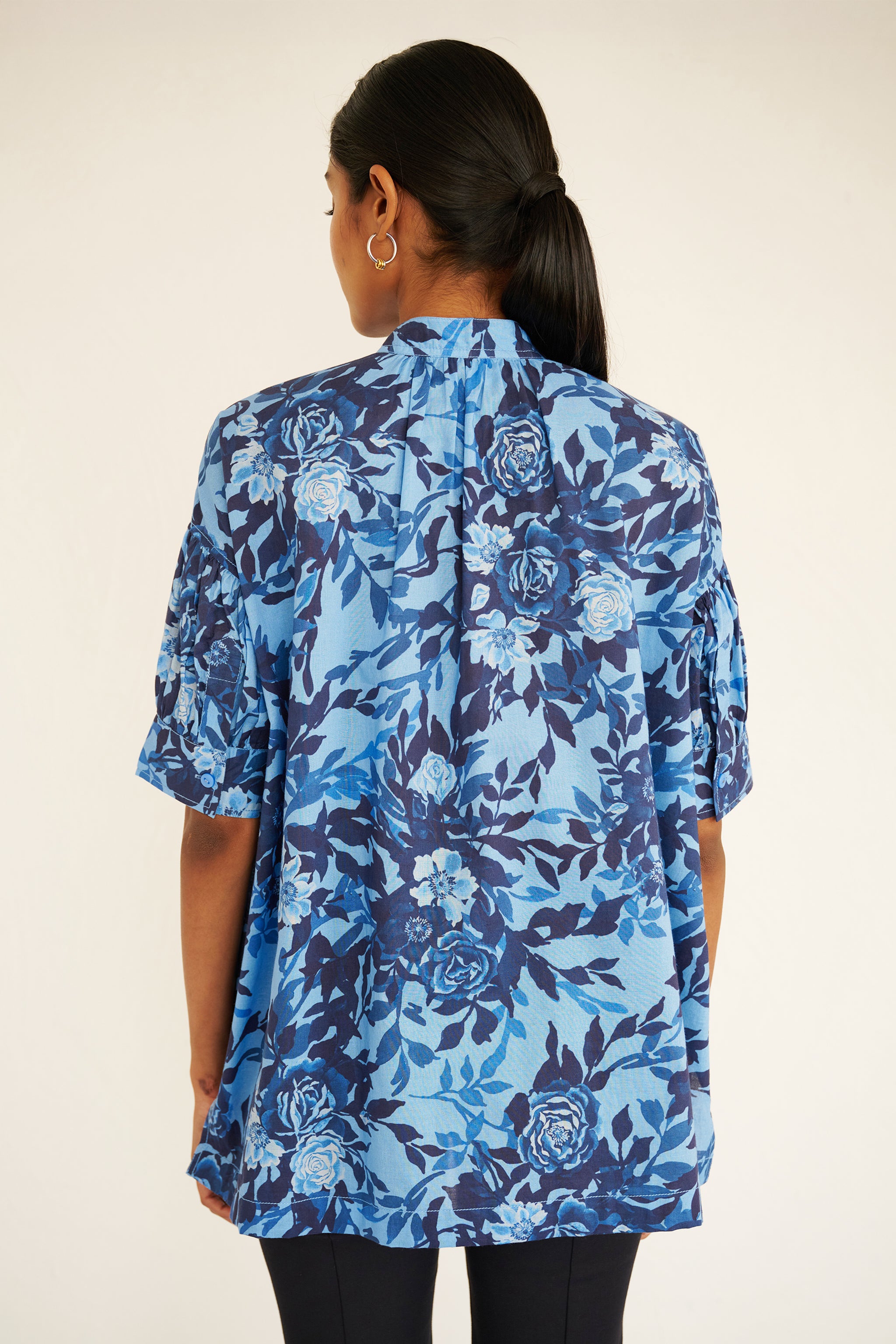 Back view of woman wearing a relaxed floral button-down shirt with drop shoulders, stand collar, and gathered neckline.