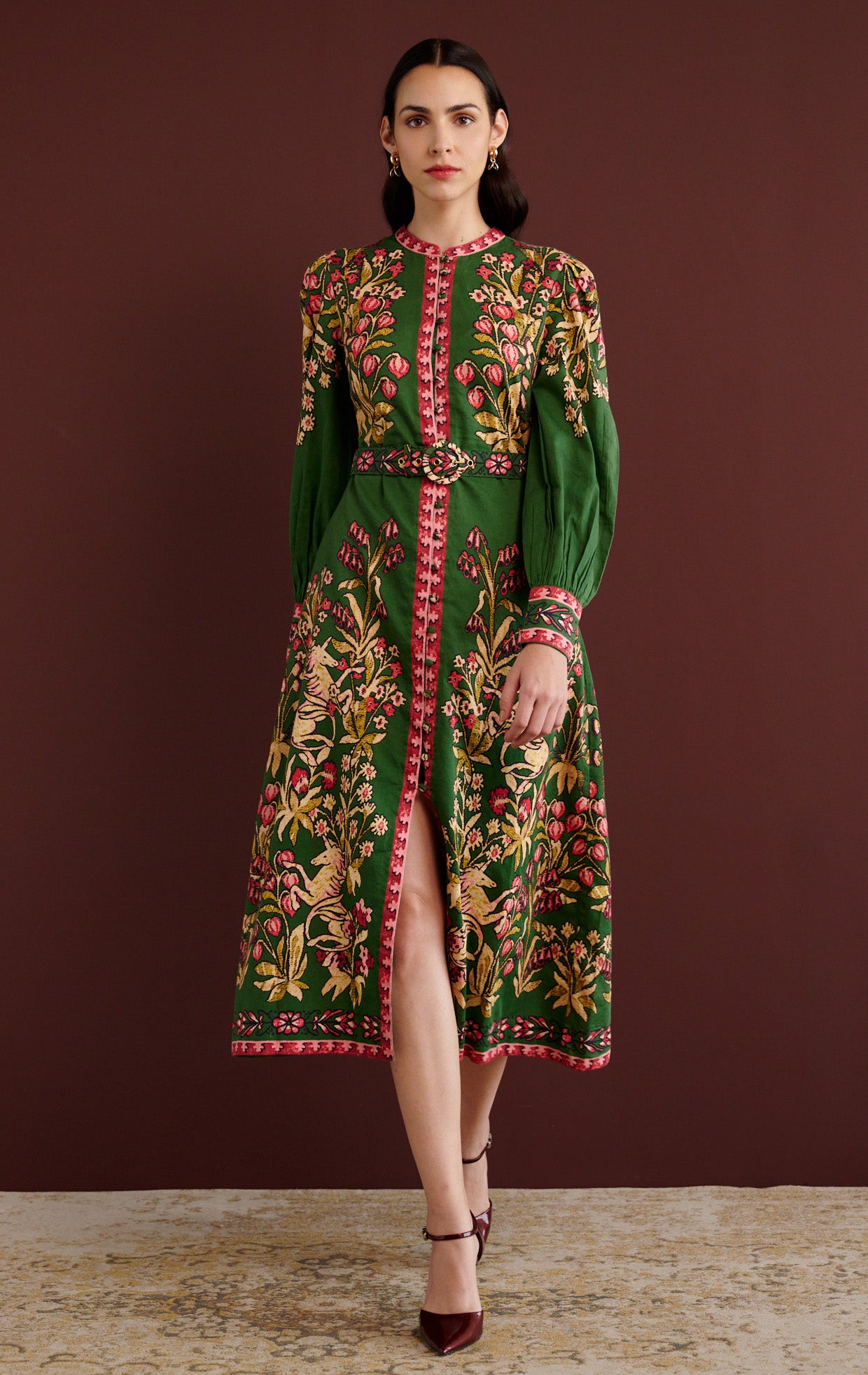 Front view of woman walking. She is wearing the Kay midi dress in Unicorn Tapestry print. It has a fitted bodice, stand collar, fabric-covered buttons, detachable belt, side-seam pockets, and 15th-century-inspired enchanted garden motifs on the shoulders and skirt.