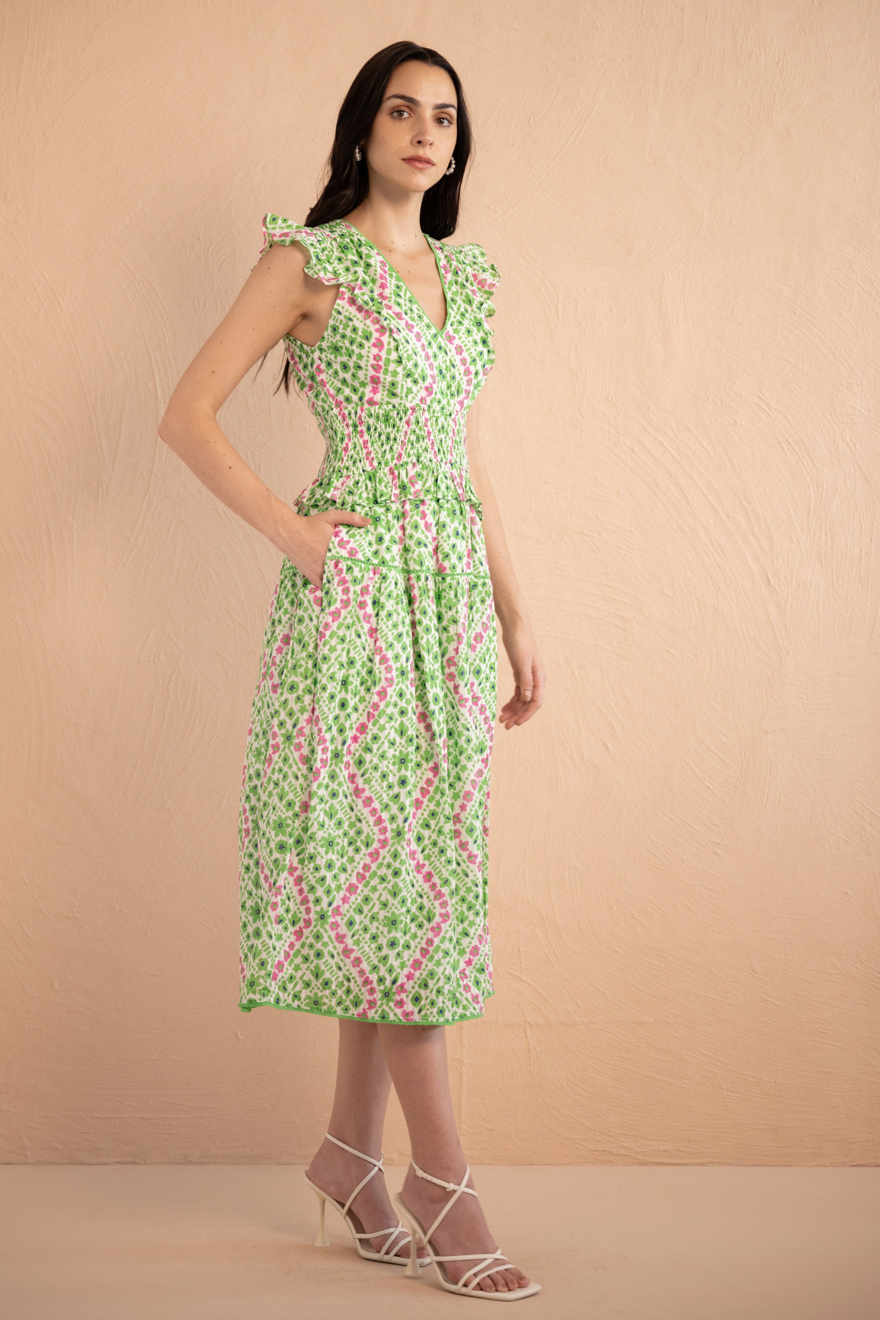 Side view of the Keira dress in a fresh green and pink Athena Heart print with floral and heart motifs. The dress features lace trim along the neckline and sleeves, a smocked waist for a flattering fit, and soft frill accents. The A-line skirt falls to the shin, and the dress includes discreet side pockets.