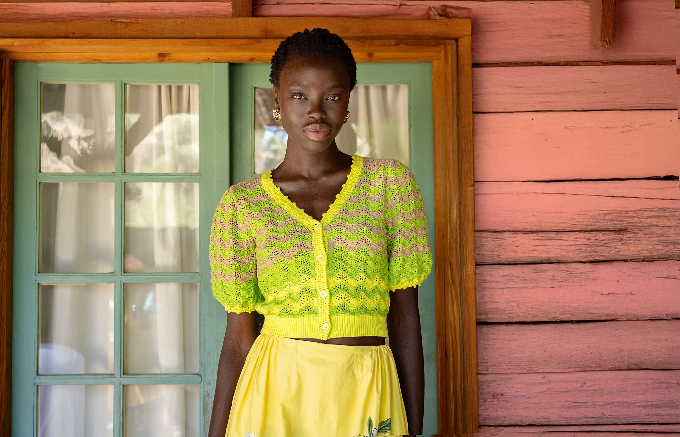 A model standing wearing Kate Chevron Cardigan in Chive color paired with Magdalena Skirt from our Spring 25 collection.