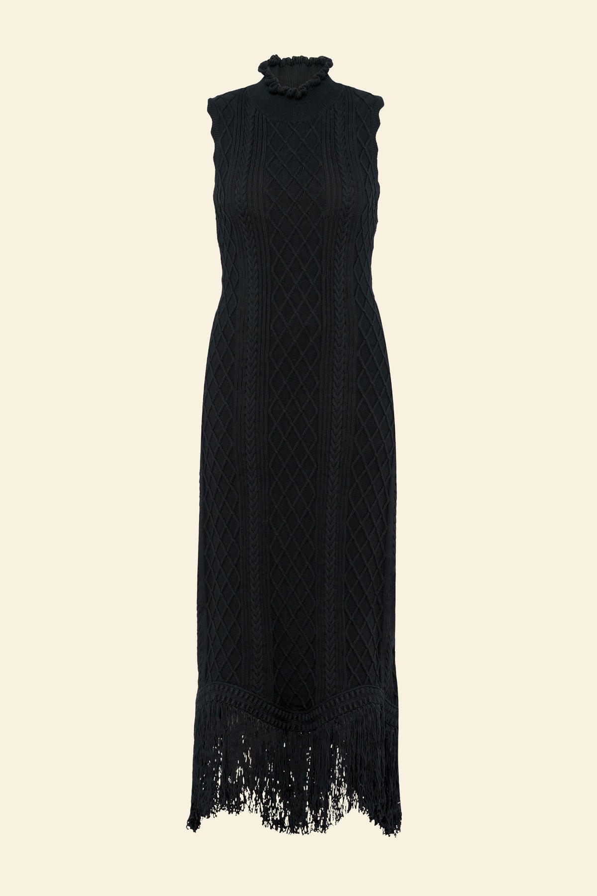 Front view product image of model standing wearing the Amelia Fringe Dress, featuring a body-skimming cable-knit silhouette, high neckline with hand-crocheted trim, and an uneven hem finished with fringe.