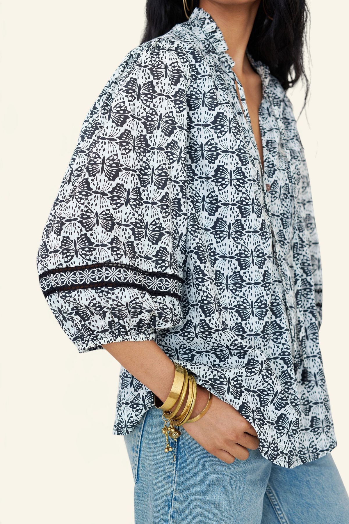 Side view close up of a woman standing wearing the Lorna top in Flutter print, featuring Celtic-knot lace sleeve inserts, and a loose cotton voile silhouette styled with jeans