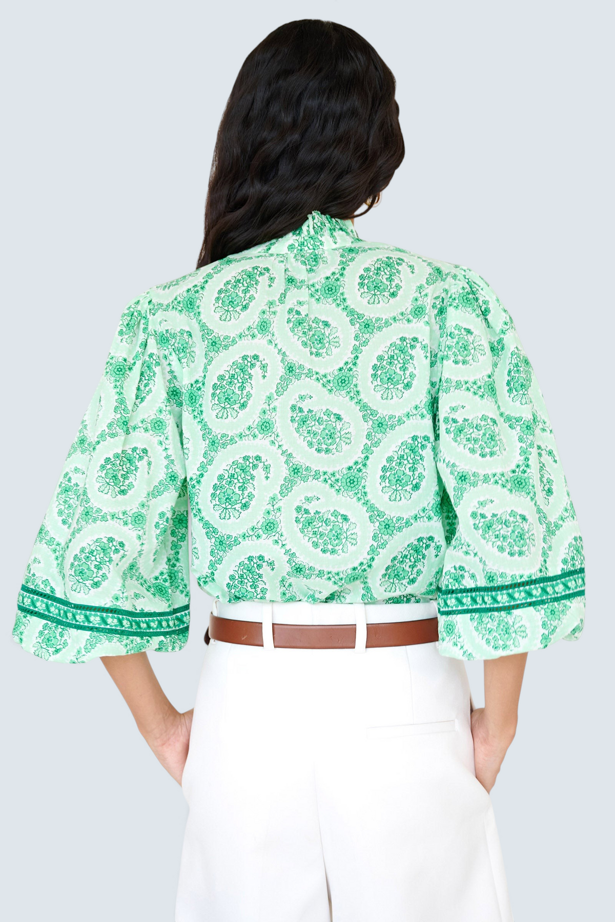 Back view closeup of a woman standing. She is wearing the Lorna top in Paisley Copse print, featuring a ruffled V-neck with tie & contrast sleeve trim.