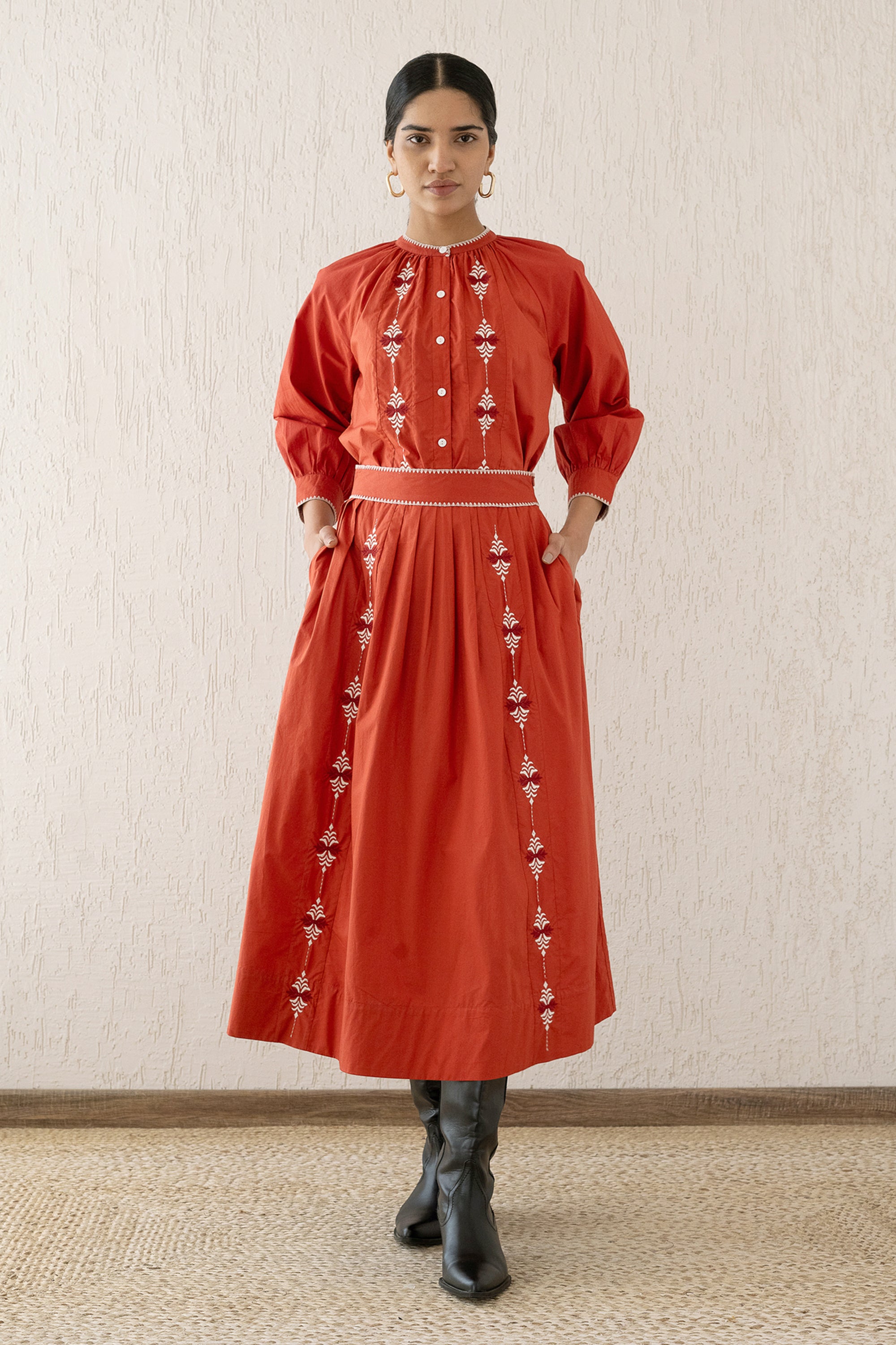 Front view of a woman wearing the Magdalena Skirt Sacher Rooibos with hands in pockets, featuring exquisite embroidery inspired by Austrian folk art, side pockets, and a side zipper fastening.