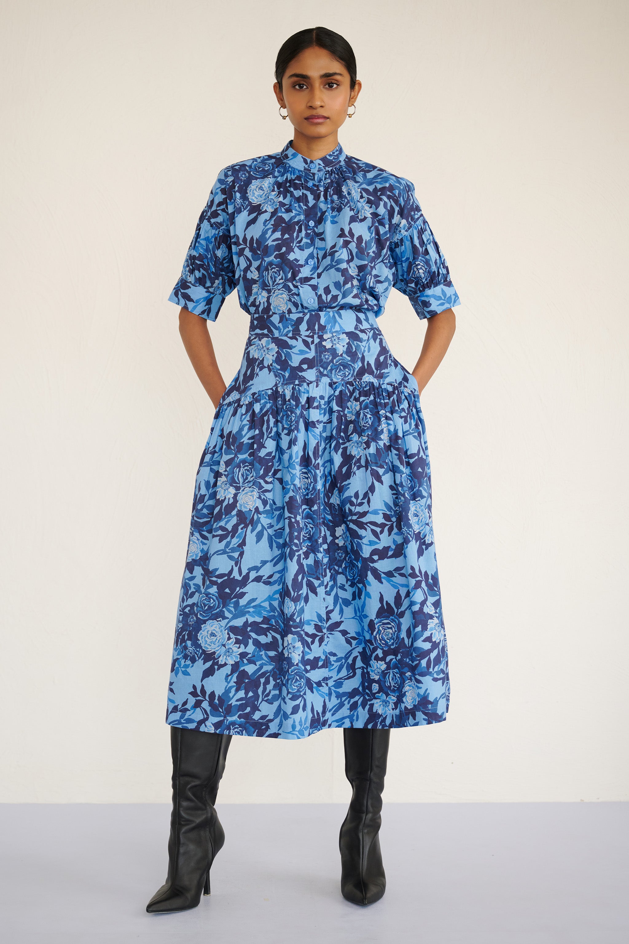 Front view of woman wearing a high-waisted floral midi skirt with a gathered silhouette and side pockets, featuring a soft watercolor rose print paired with Ivy shirt in same print.