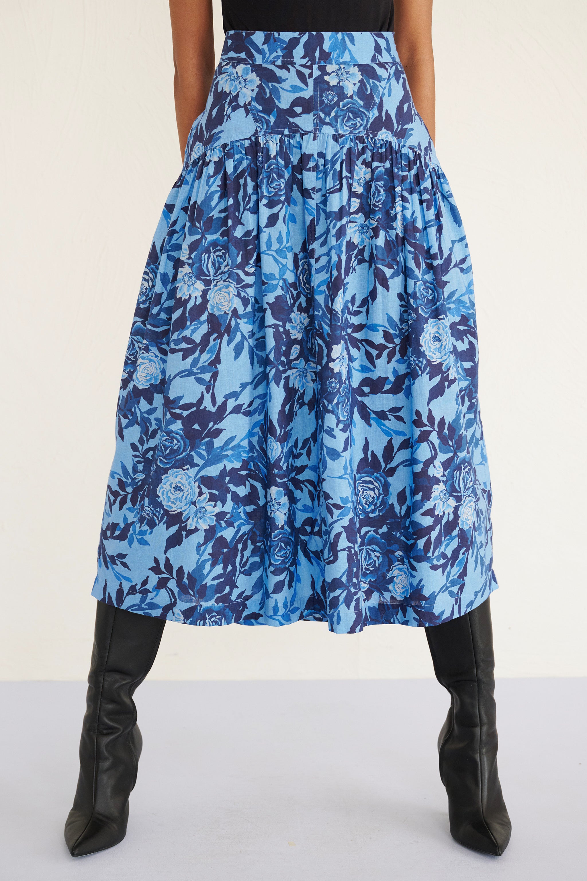 Front view of woman wearing a high-waisted floral midi skirt with a gathered silhouette and side pockets, featuring a soft watercolor rose print.