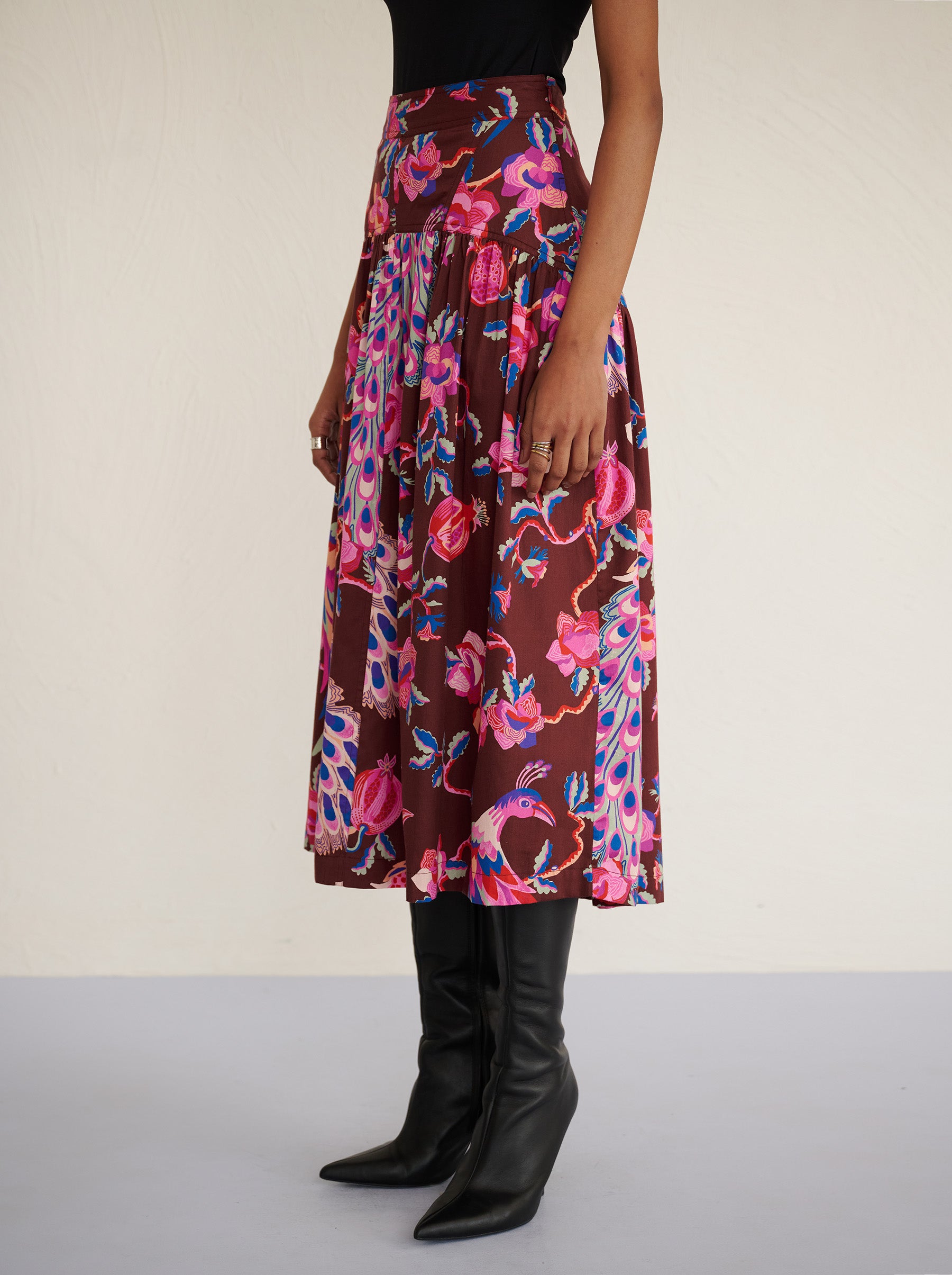 Side view close up of a model standing. She is wearing the Melodie skirt in cotton sateen with the Bukhara Peacock print in rum color. It is slim at the waist and gathered below for a flattering shape. The skirt is fully lined with side-seam pockets.