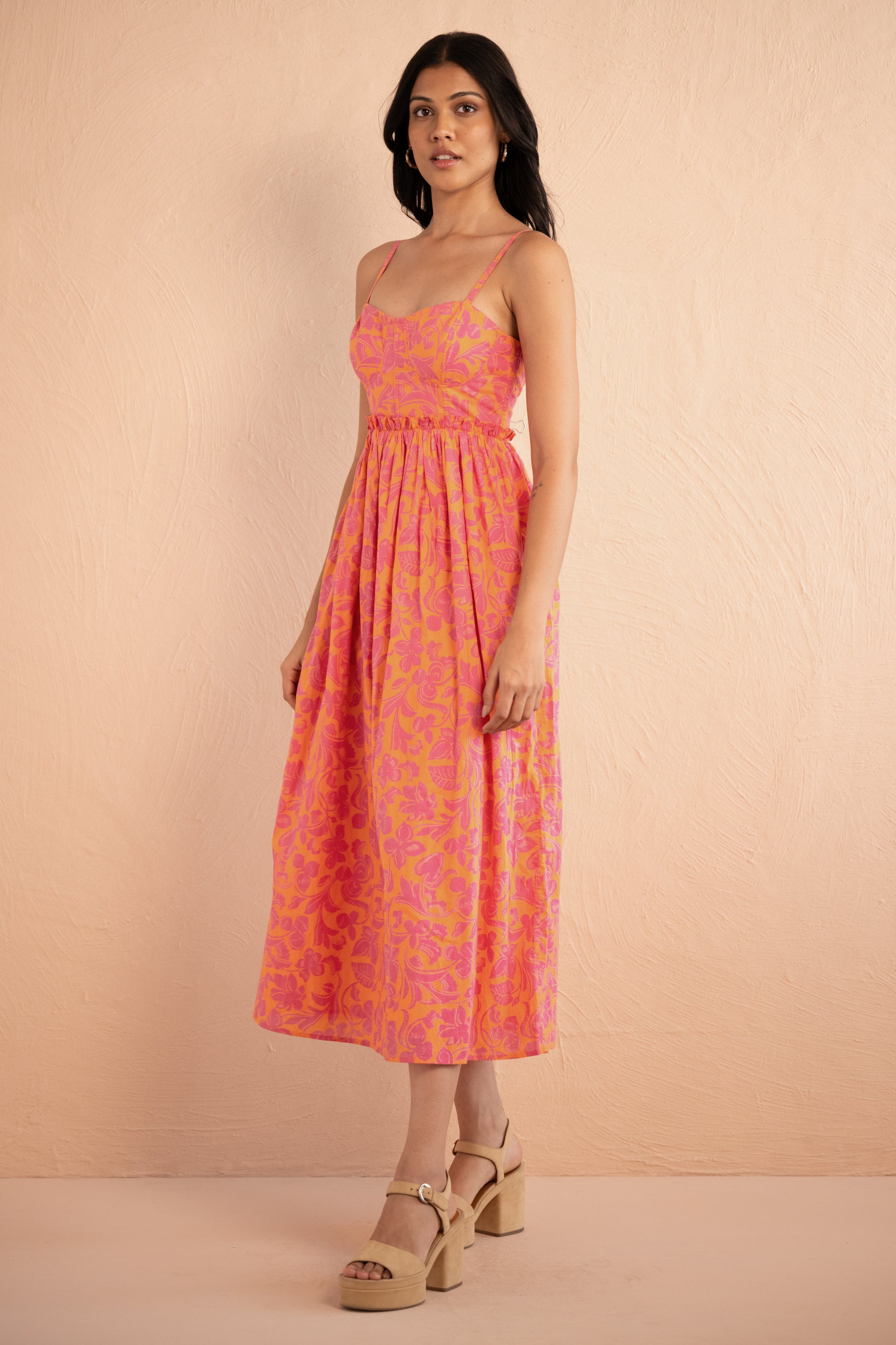 Side view of woman wearing Phoebe Dress in Gaia Nectarine print, featuring corset bust detailing, gathered waist, full skirt, and side-seam pockets in bold sunset floral cotton voile.