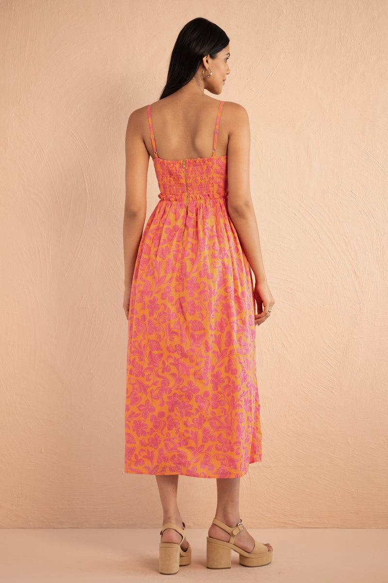 Back view of woman wearing Phoebe Dress in Gaia Nectarine print, featuring corset bust detailing, gathered waist, full skirt, and side-seam pockets in bold sunset floral cotton voile.