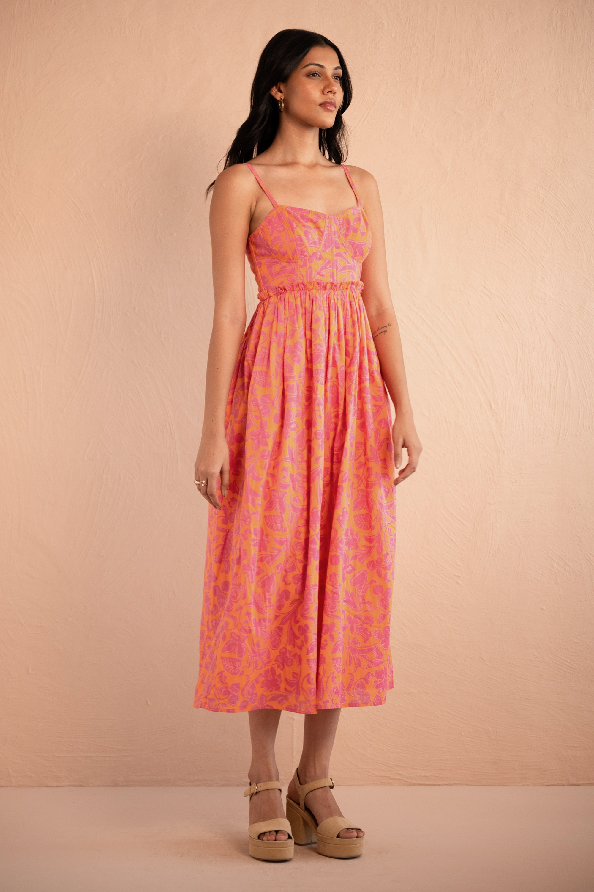 Front view of woman wearing Phoebe Dress in Gaia Nectarine print, featuring corset bust detailing, gathered waist, full skirt, and side-seam pockets in bold sunset floral cotton voile.