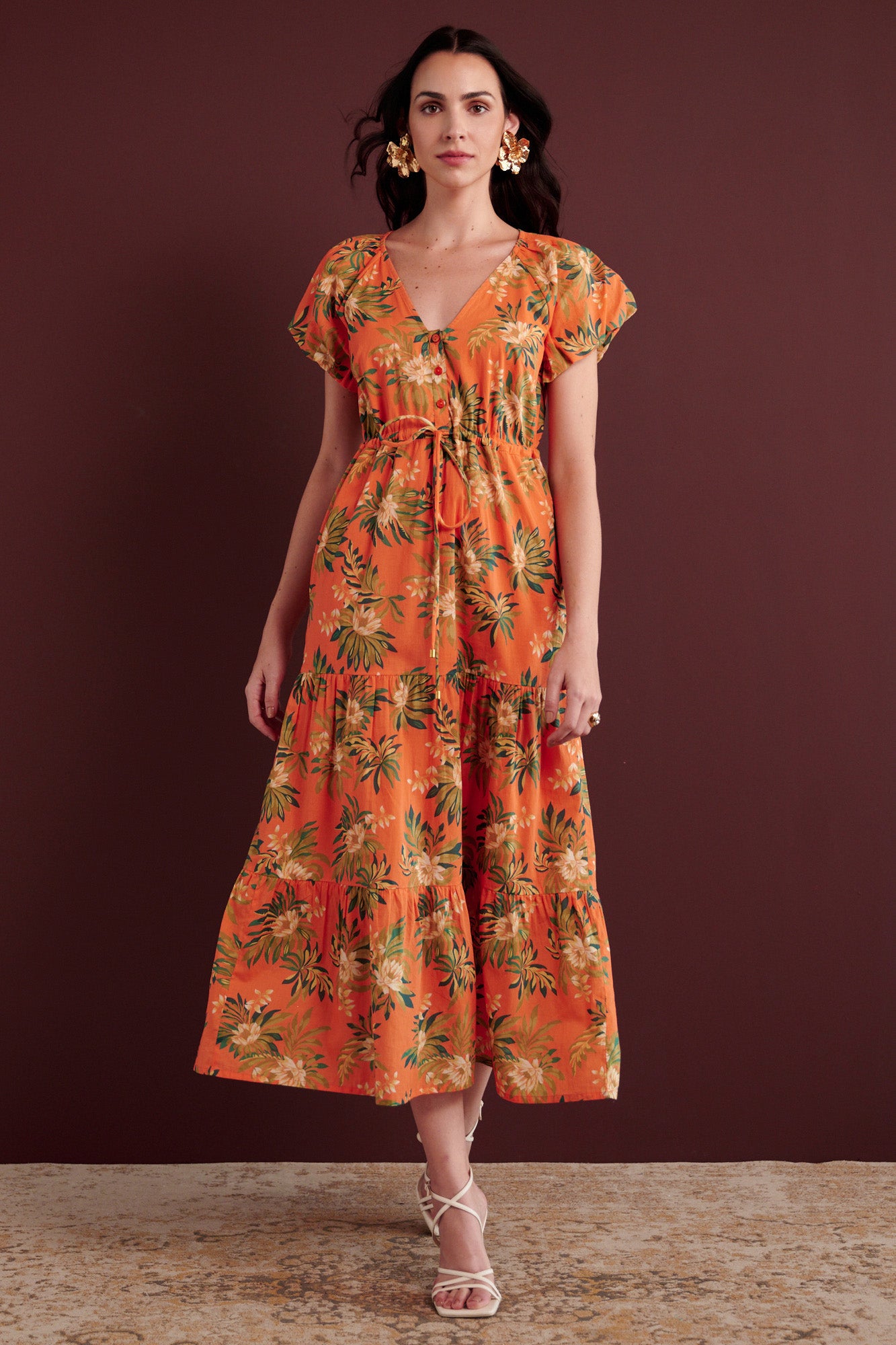 Back view of woman walking. She is wearing the Poppy dress in Artichoke Flower print. It has a raglan blouson sleeves, front button placket, drawstring waist, flowing skirt, cap sleeves, fully lined construction, and side-seam pockets.