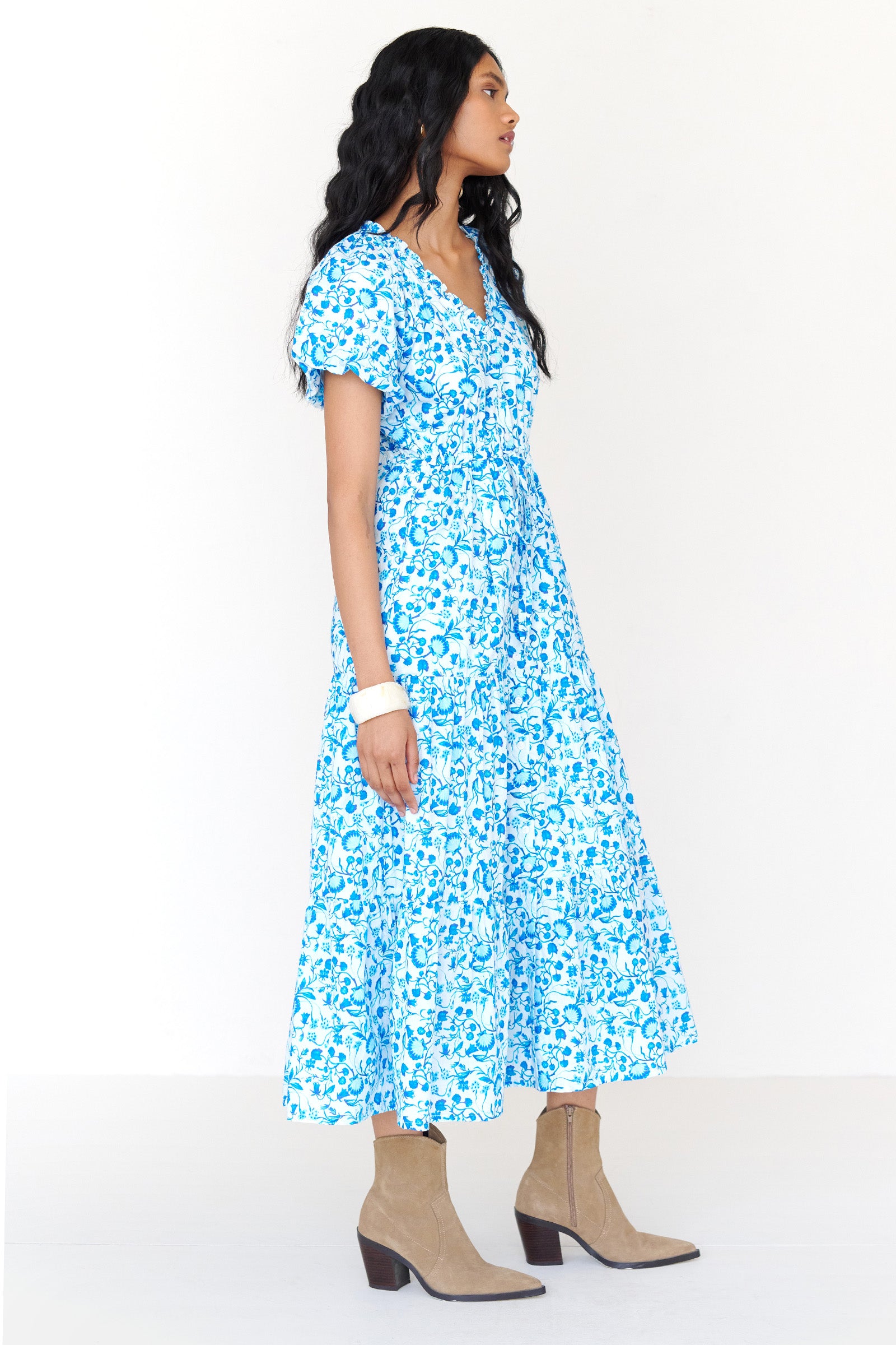 Side view of a woman standing wearing the Poppy dress in Clam Garland print. It features raglan blouson sleeves, front button placket, drawstring waist, flowing skirt and side-seam pockets.