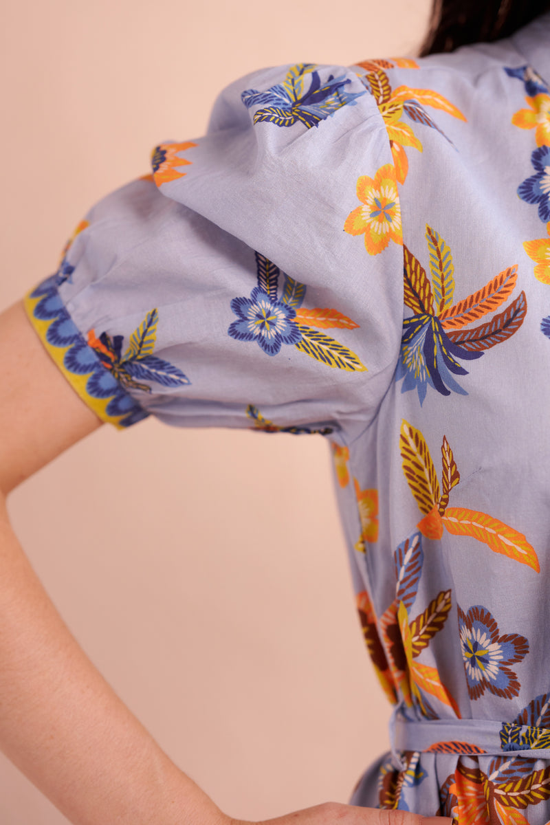 Close-up of puff sleeve with gathered seam and floral print in blue, yellow, and orange on light blue cotton fabric.